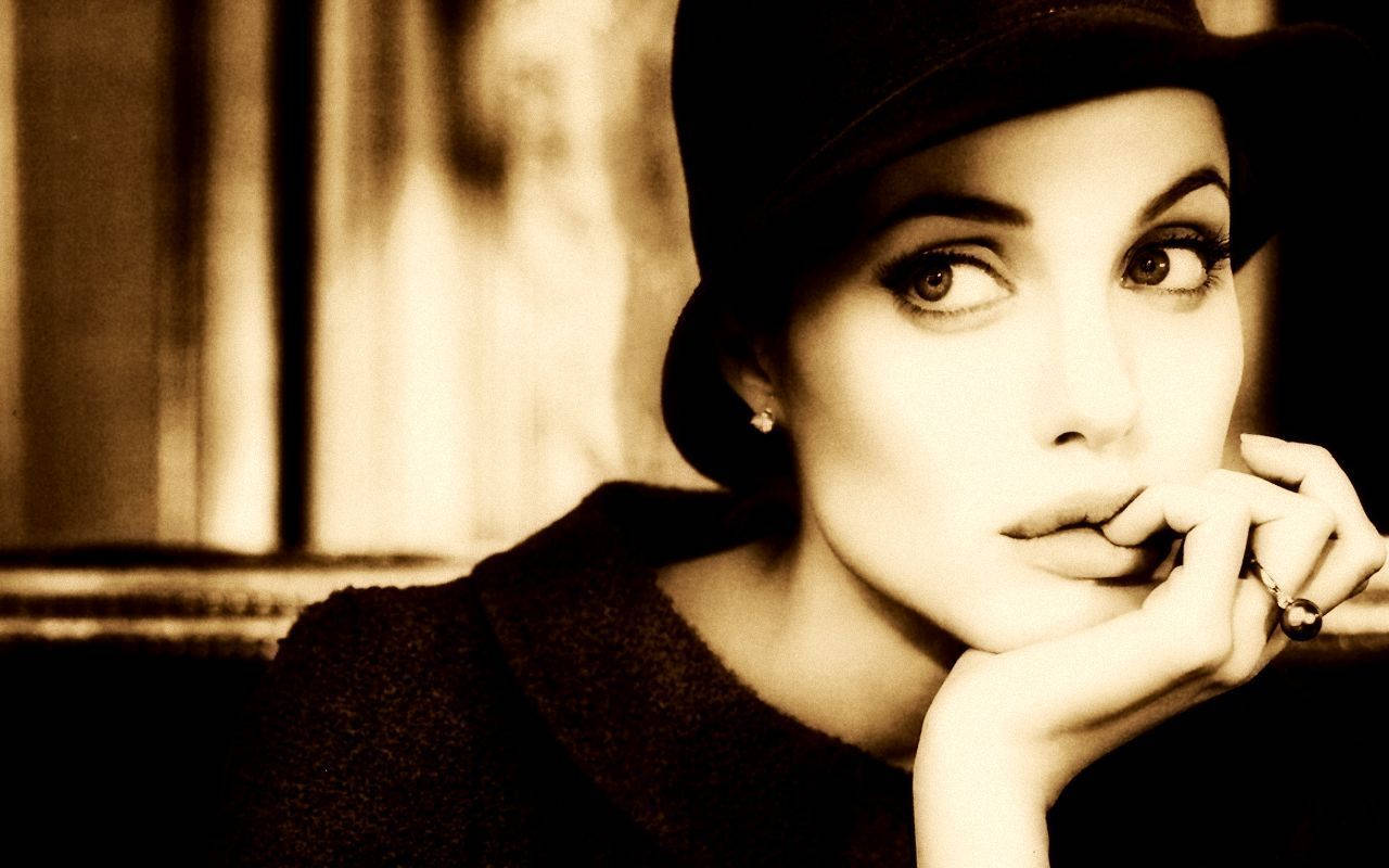 Angelina 桌布 壁紙 — 一位戴黑色帽子的女士，手托下巴，若有所思地凝視著模糊的懷舊色背景。