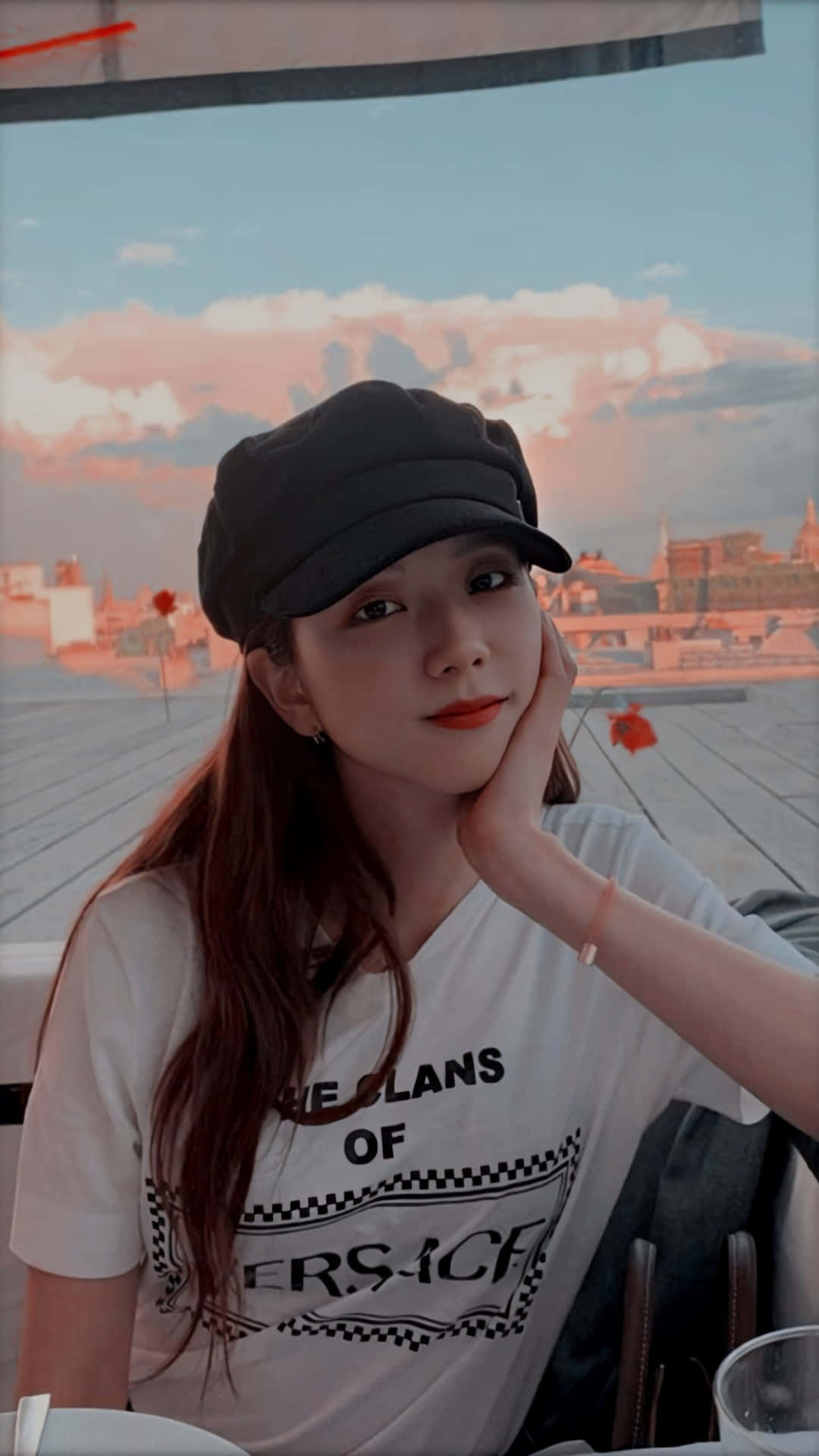 BLACKPINK 桌布 壁紙 — 一位戴黑色帽子的年輕女子，在夕陽城市景觀背景下，將下巴擱在手上。