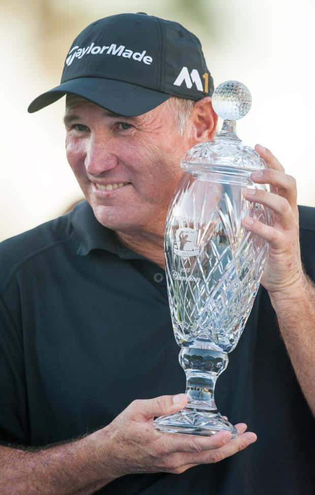 Trophy 桌布 壁紙 — 一位戴黑色帽子的微笑高爾夫球手自豪地舉起一個頂部有高爾夫球的大型水晶獎盃。