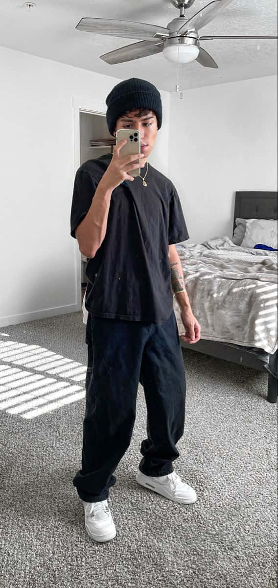 美學 桌布 壁紙 — 一位戴黑色毛帽、身穿寬鬆衣服的年輕男子，在鋪有陽光條紋地毯的極簡主義臥室裡對著鏡子自拍。