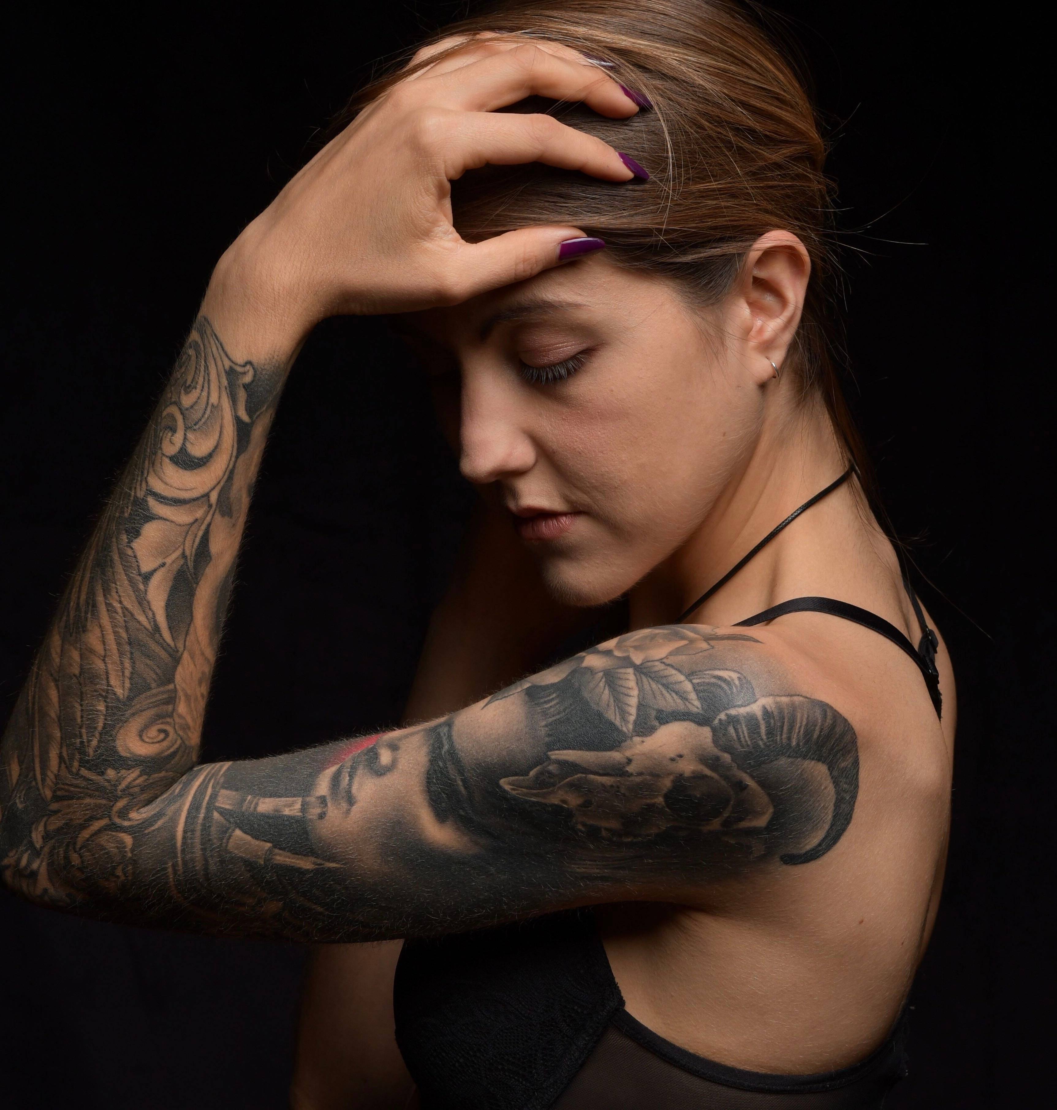 Woman 桌布 壁紙 — 一位手臂和肩膀上有複雜黑色刺青的女性，在深色背景前將手放在頭上。