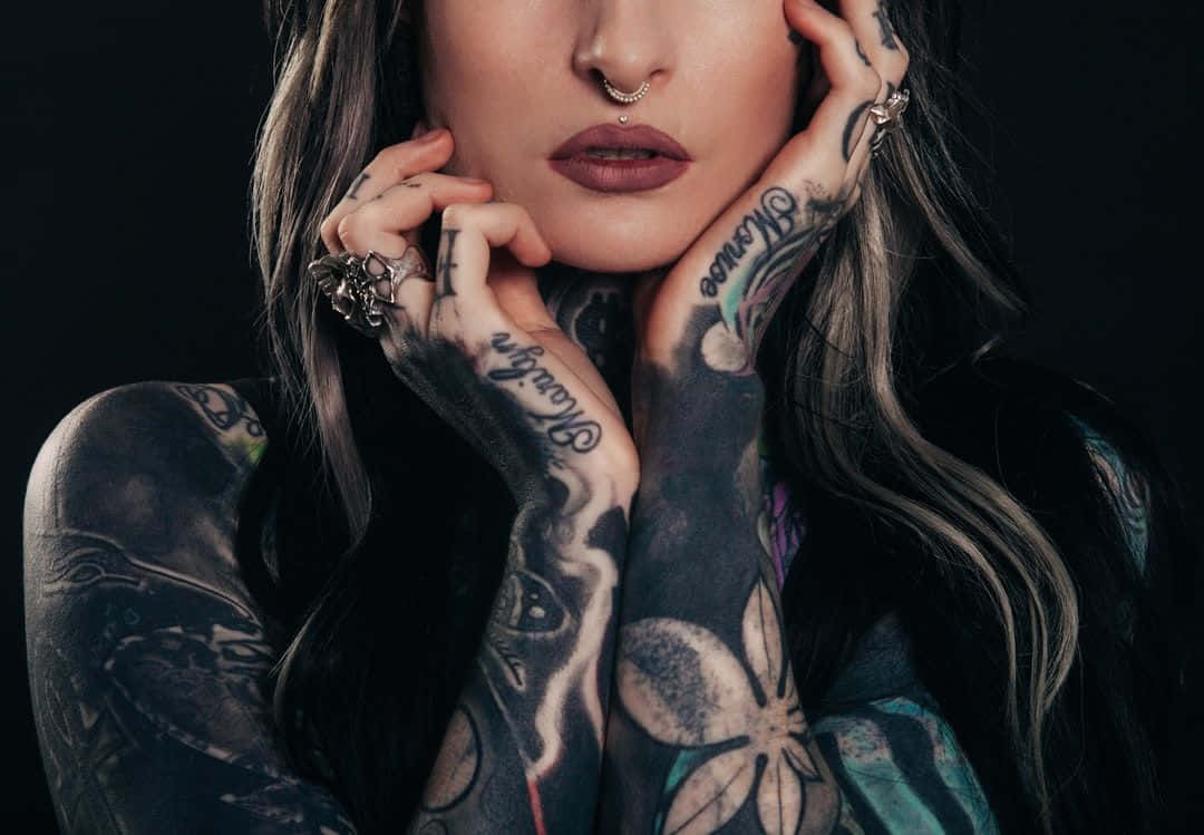 Tattoo 桌布 壁紙 — 一位手臂和雙手佈滿刺青的女性，在黑色背景前將下巴擱在手掌上。