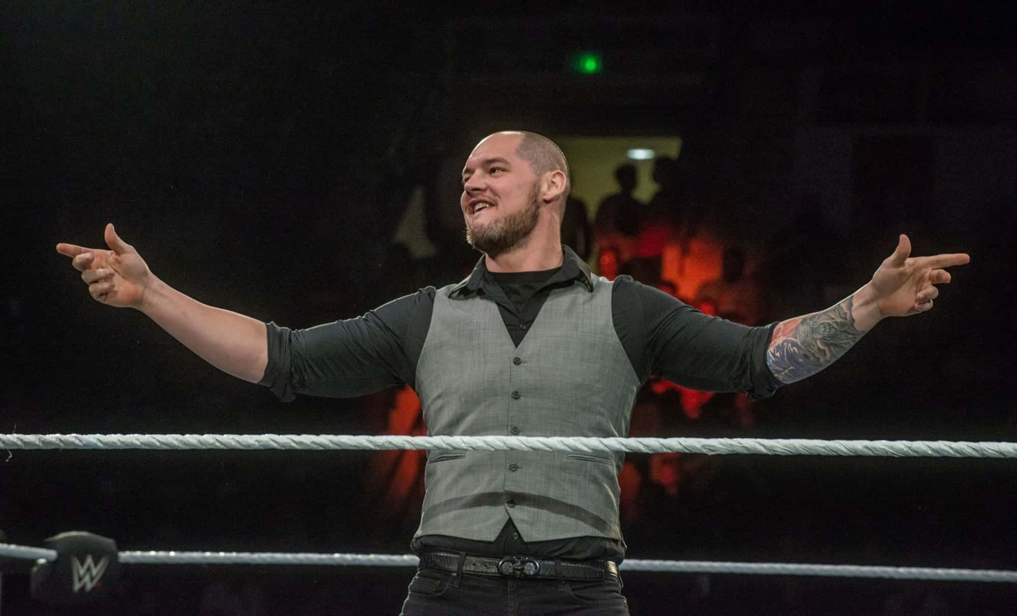 WWE 桌布 壁紙 — 一位手臂有刺青、留鬍子的摔角選手在摔角場中張開雙臂，勝利地指向觀眾。