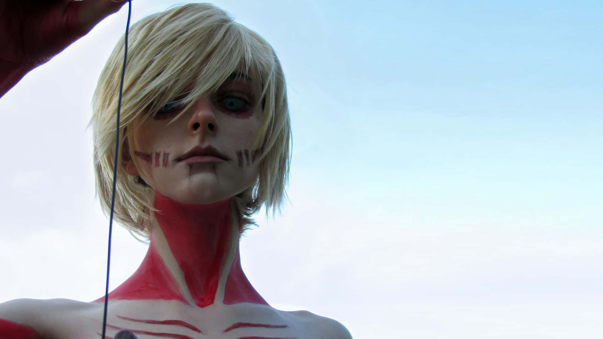 Female Titan 桌布 壁紙 — 一位扮演《進擊的巨人》中巨人的角色扮演者，金髮，紅色肌肉紋理，背景是蒼白的天空。
