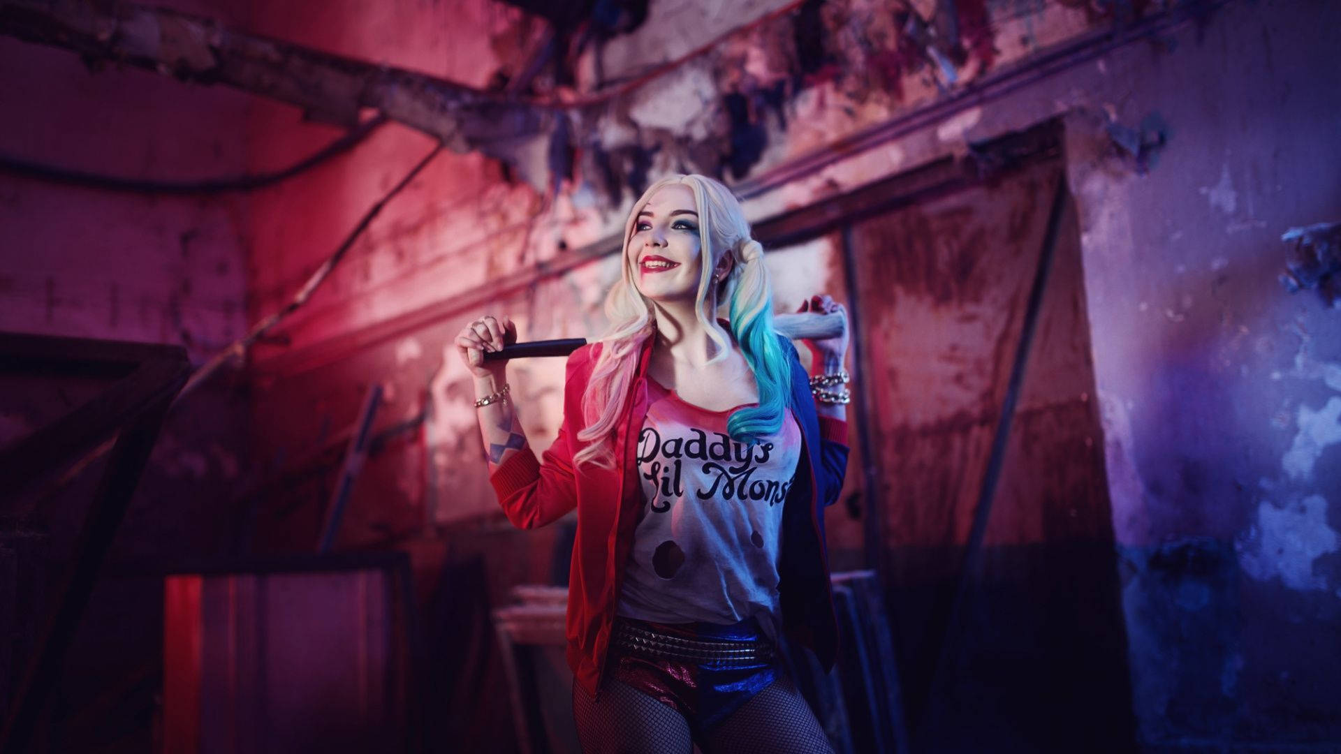 Harley 桌布 壁紙 — 一位扮演哈莉·奎茵的角色扮演者自信地站在廢墟建築中，手持棒球棍，在戲劇性的紅藍燈光下。