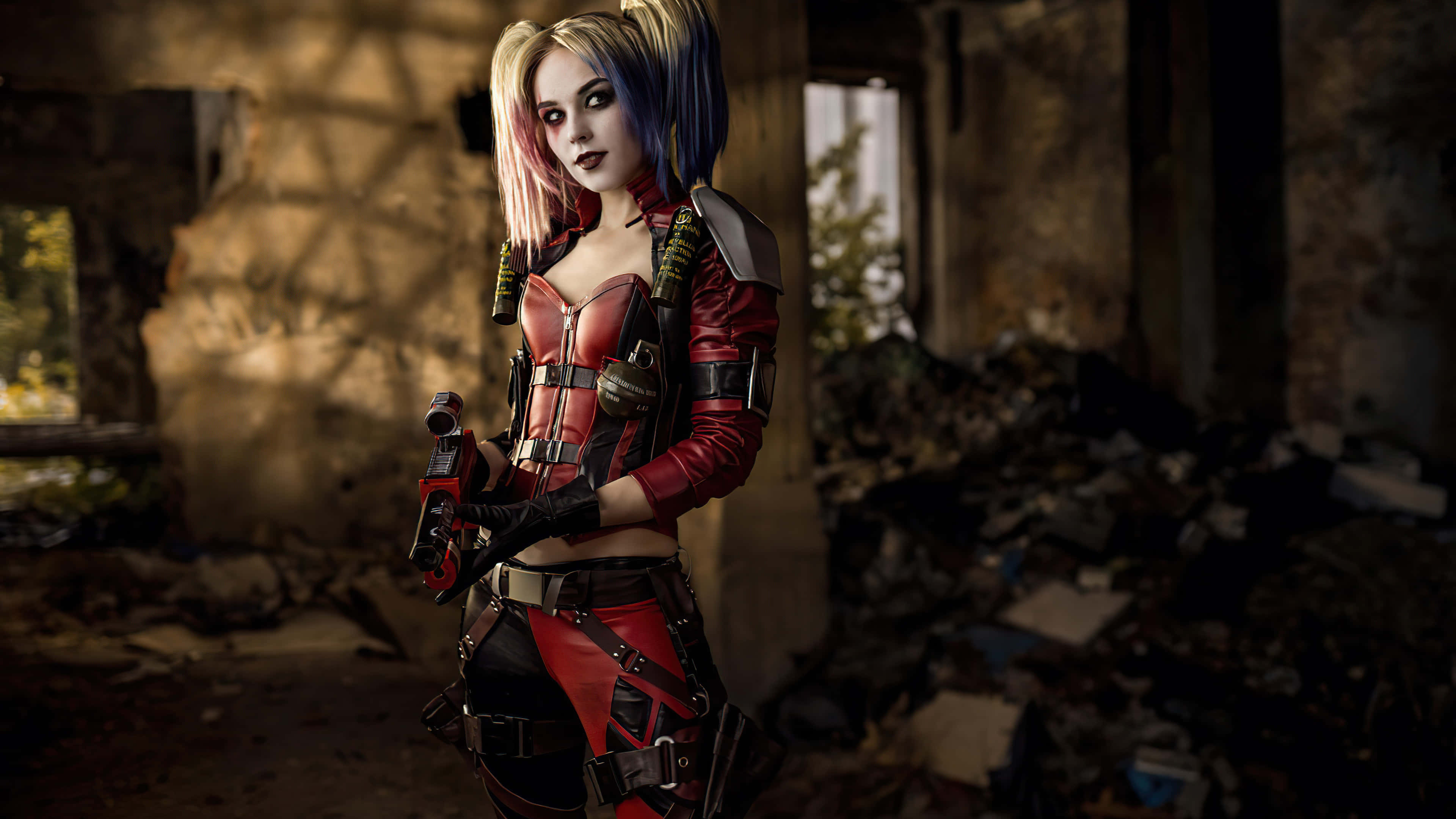 Harley Quinn Cosplay 桌布 壁紙 — 一位扮演哈莉·奎茵的角色扮演者自信地站在陽光照射的廢棄建築物中，手持武器。