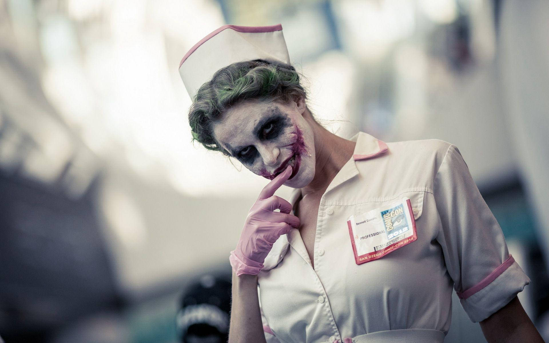 job 桌布 壁紙 — 一位扮演小丑護士的cosplayer，綠色頭髮、白色臉部彩繪和粉紅色手套，手指放在嘴唇上擺姿勢。