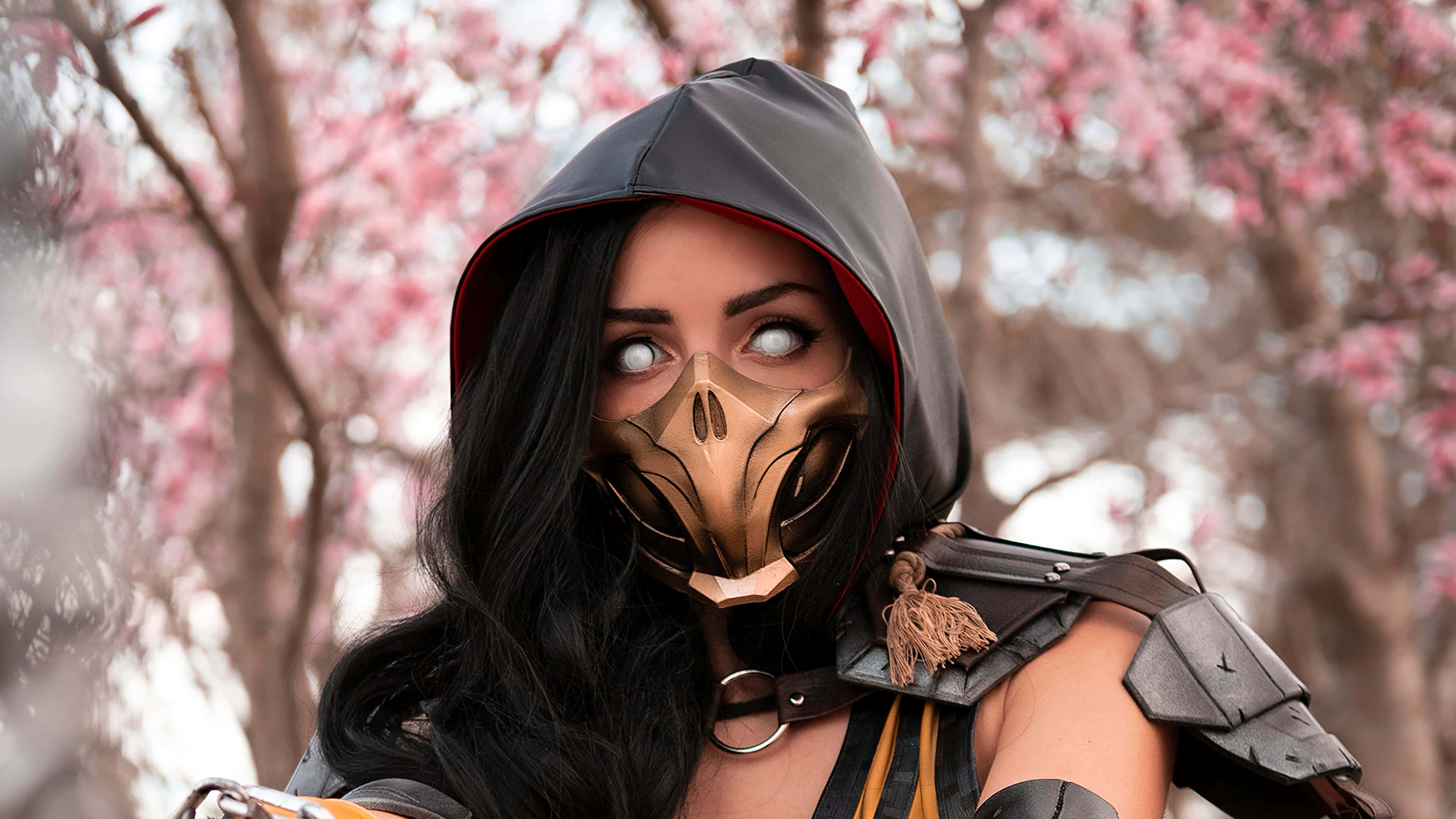 Gaming Cosplay 桌布 壁紙 — 一位扮演蠍子的角色扮演者，戴著精細的蠍子面具和連帽盔甲，在柔和的粉紅色櫻花背景下擺姿勢。