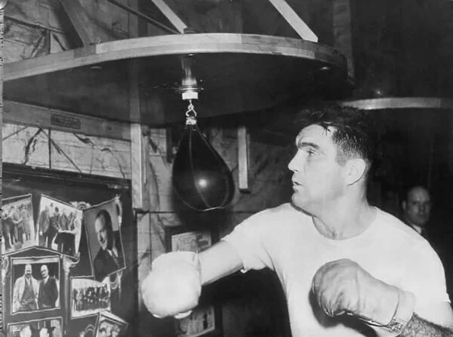 Boxing 桌布 壁紙 — 一位拳擊手在復古健身房中，在昏暗燈光下擊打速度球，身後牆上掛著裱框照片。