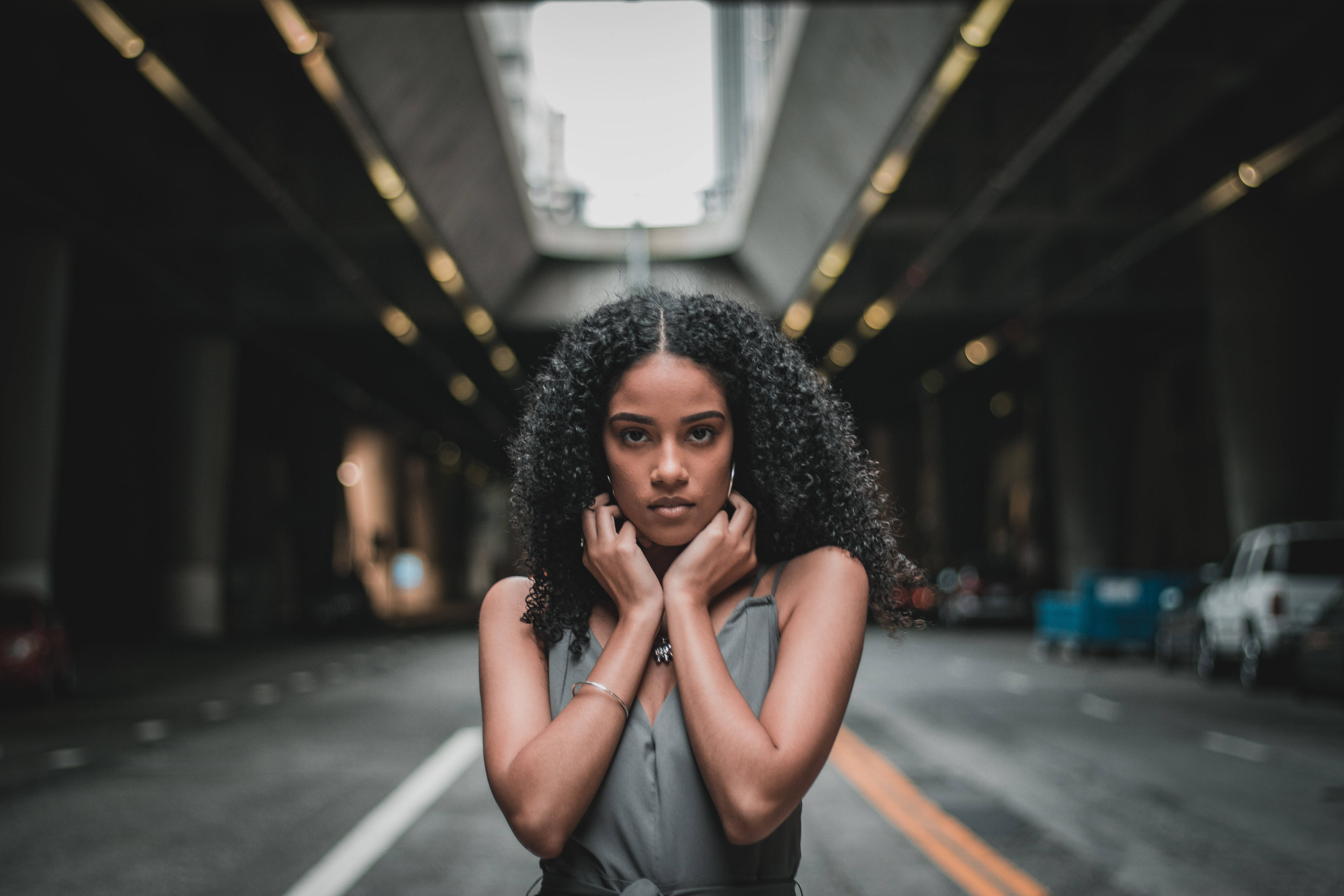 Black Girl 桌布 壁紙 — 一位捲髮女士站在昏暗的城市隧道中，雙手靠近臉部，直視鏡頭，表情嚴肅。