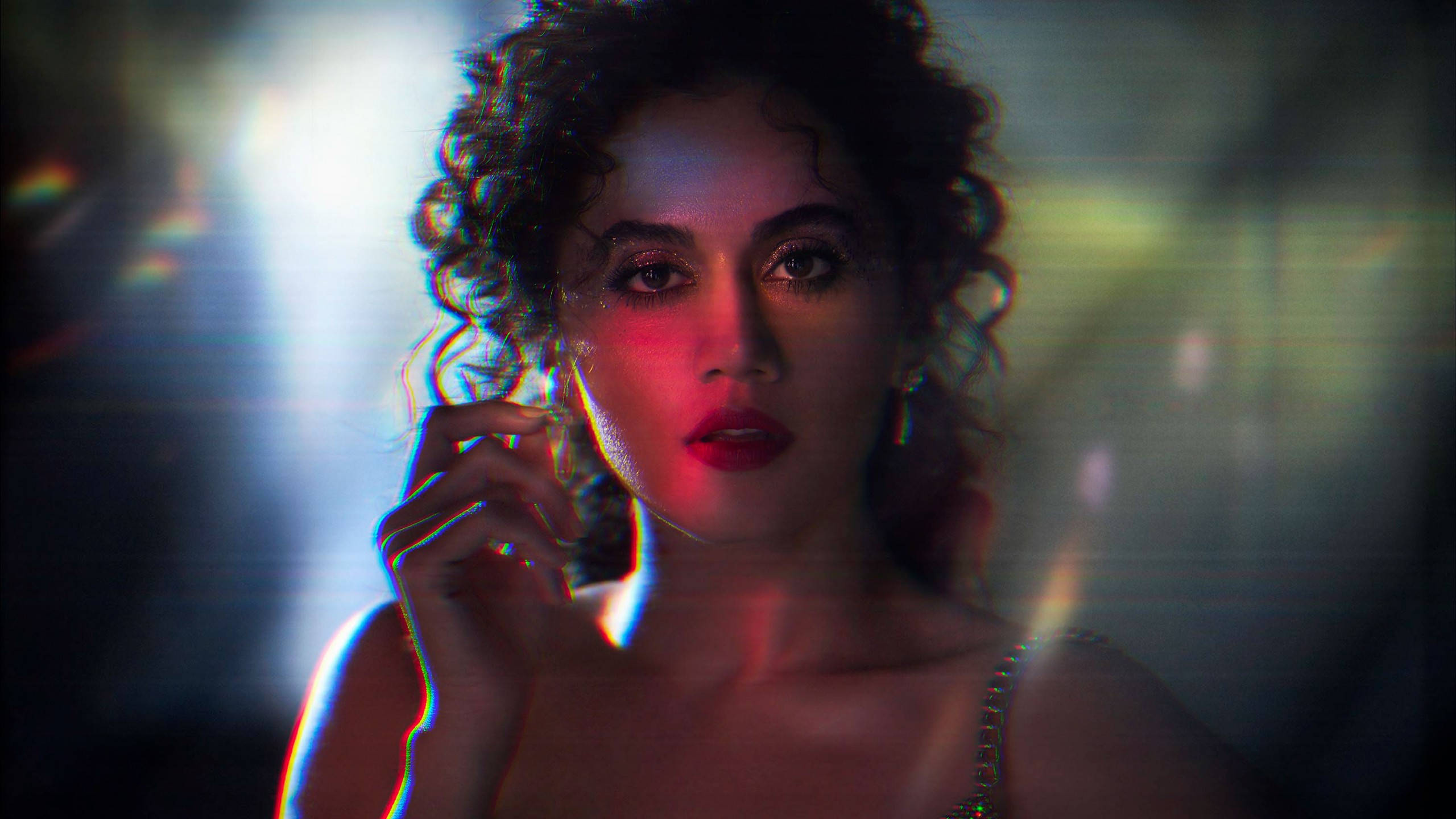 Taapsee Pannu 桌布 壁紙 — 一位捲髮女性在戲劇性的紅藍燈光及鏡頭光暈下，目光強烈地凝視。