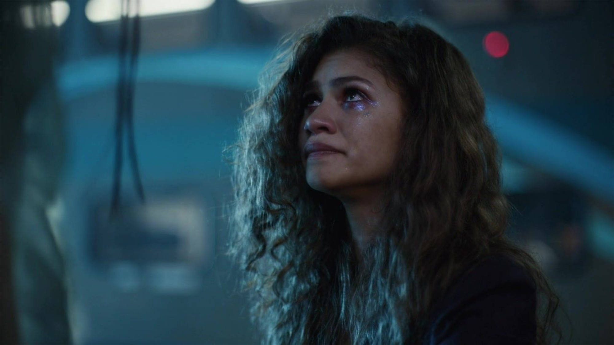 Zendaya 桌布 壁紙 — 一位捲髮女性在昏暗的未來場景中，在冷藍色燈光下哭泣。