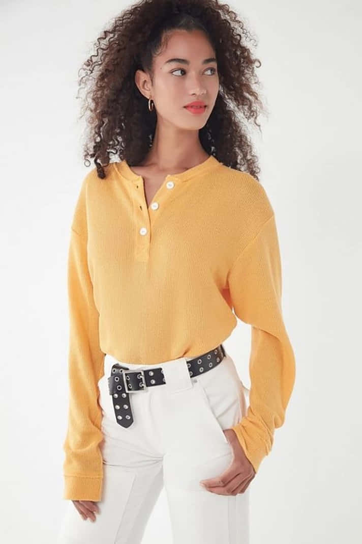 Yellow Fashion 桌布 壁紙 — 一位捲髮女性穿著芥末黃亨利衫和白色褲子，搭配鉚釘腰帶，背景為純白色。