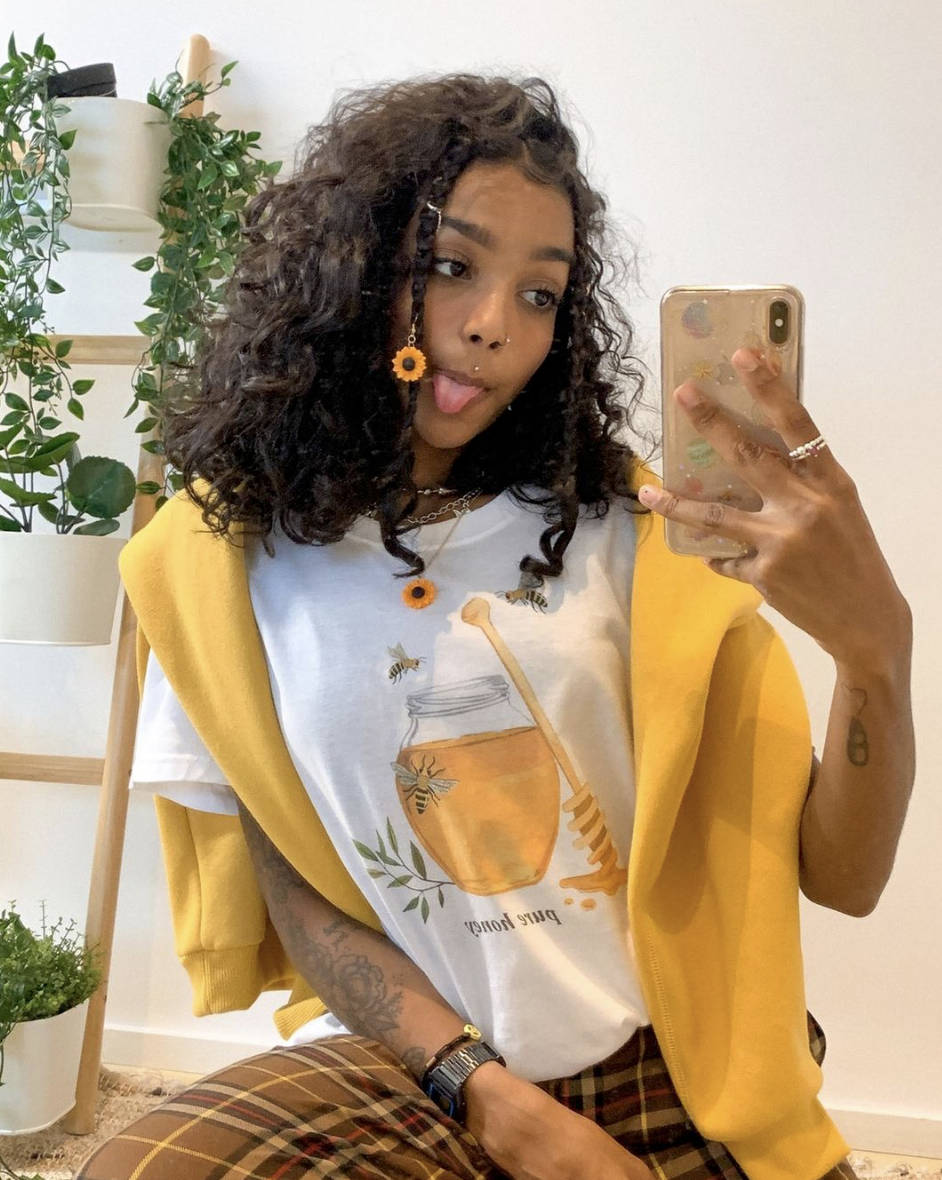 Black Girl 桌布 壁紙 — 一位捲髮年輕女性在一個有植物的明亮房間裡自拍時伸出舌頭。