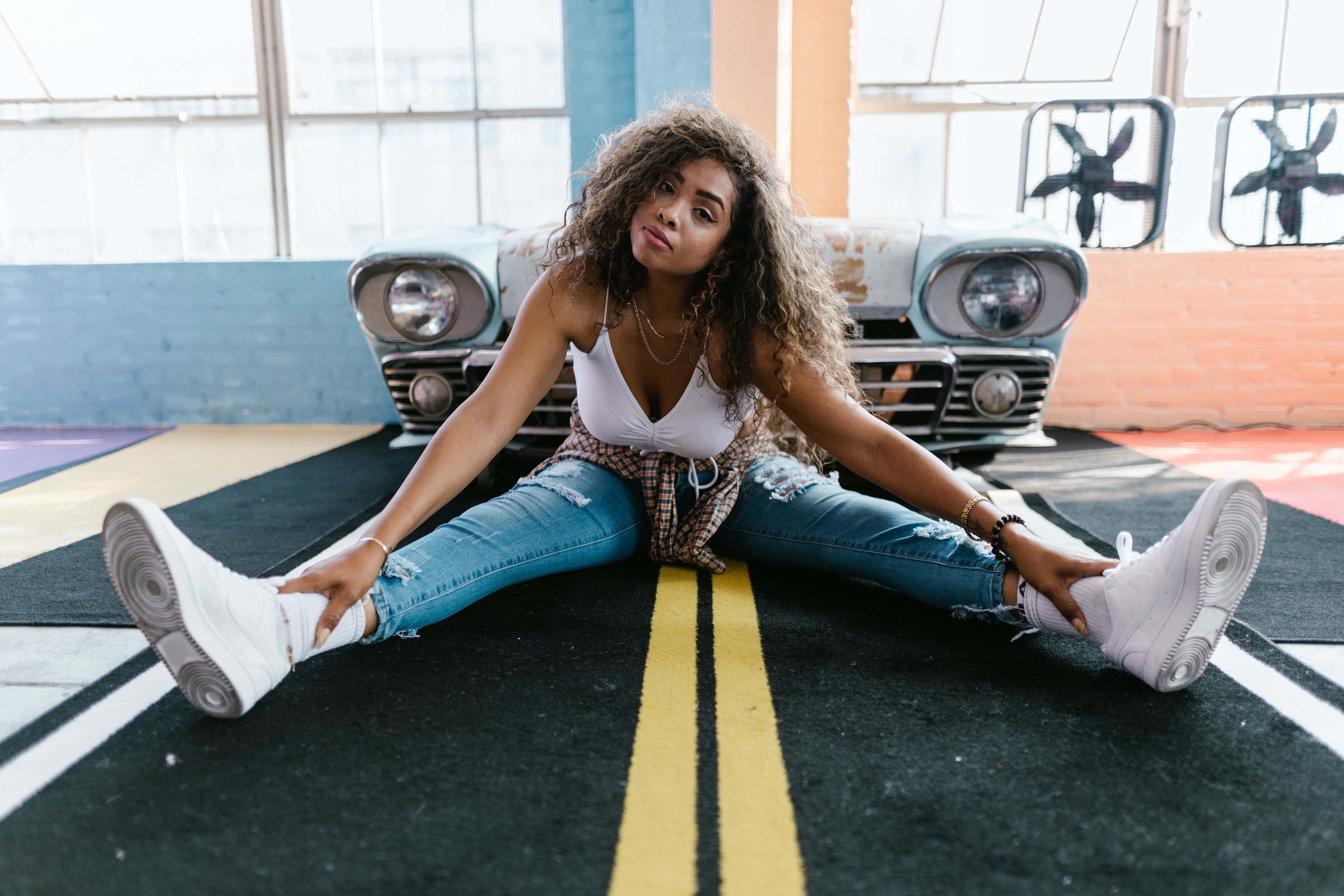 Modeling 桌布 壁紙 — 一位捲髮年輕女性坐在一輛復古車前、帶有道路圖案的地毯上，雙腿分開。