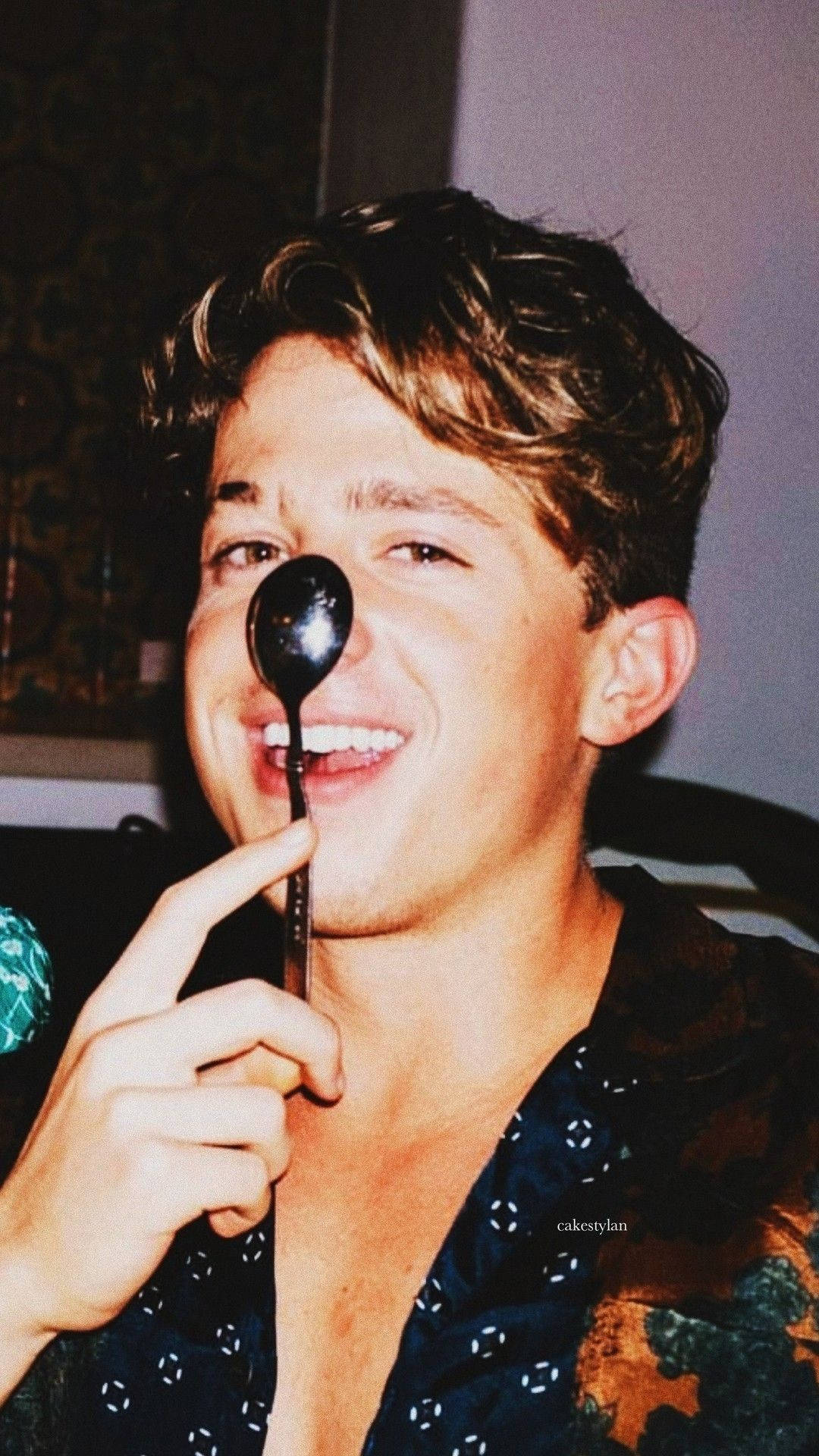 Charlie Puth 桌布 壁紙 — 一位捲髮年輕男子在溫暖的室內環境中，調皮地微笑著將湯匙放在鼻子上。
