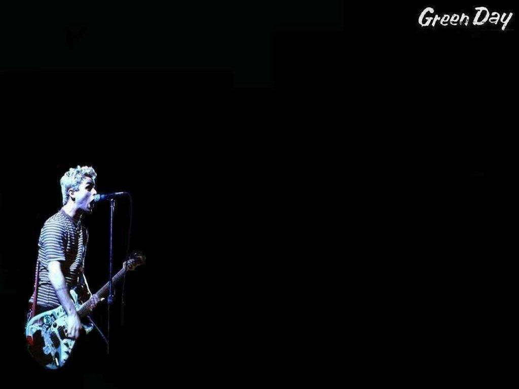 Green Day 桌布 壁紙 — 一位捲髮音樂家在黑色背景前，在戲劇性的藍色舞台燈光下，拿著吉他對著麥克風唱歌。