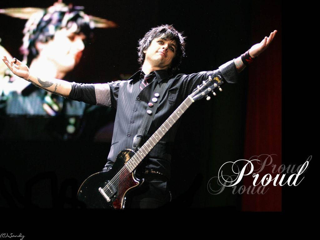 Green Day 桌布 壁紙 — 一位搖滾音樂家張開雙臂，在戲劇性的聚光燈下，手持黑色電吉他，在舞台上露出勝利的笑容。