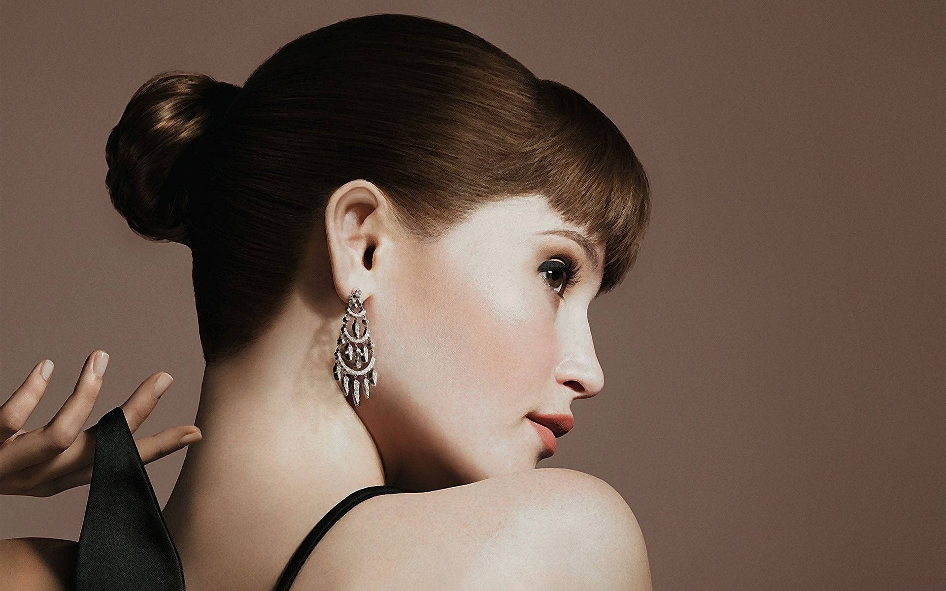 Gemma Arterton 桌布 壁紙 — 一位擁有優雅盤髮和華麗垂墜耳環的女性，在柔和的棕色背景下，若有所思地越過肩膀凝視。