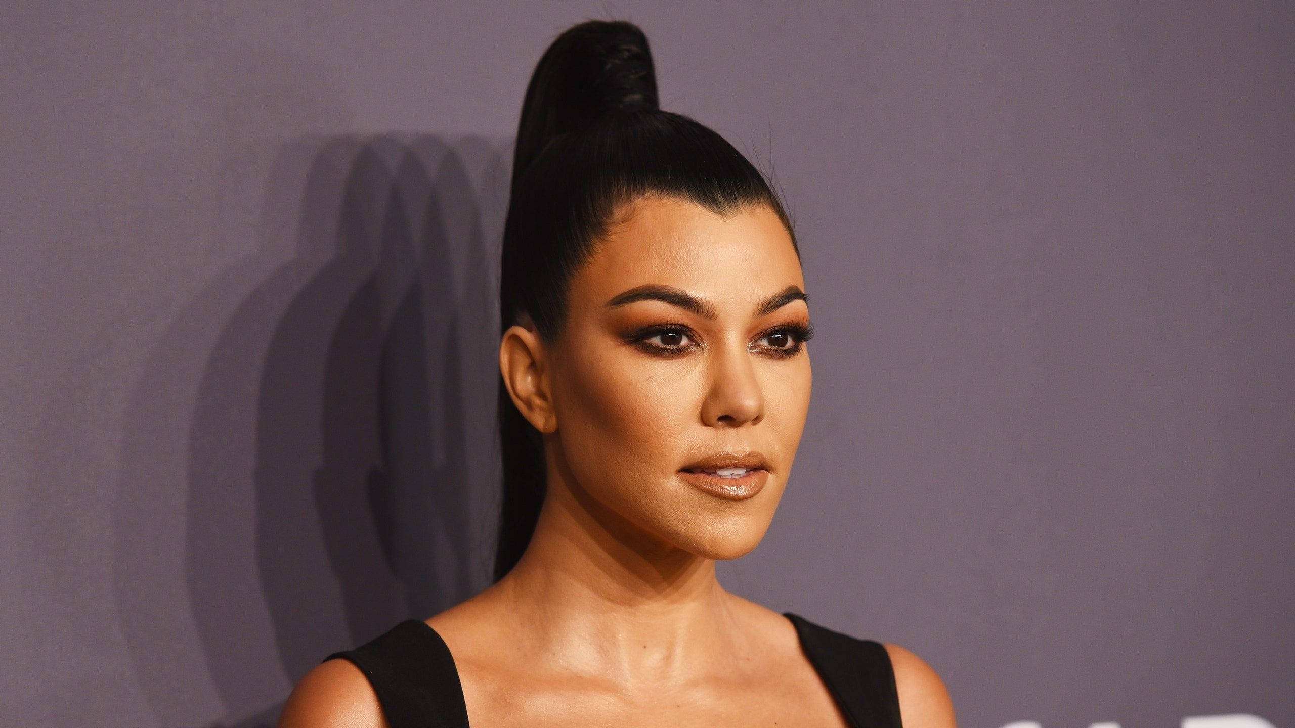 Kourtney 桌布 壁紙 — 一位擁有光滑高馬尾和誇張妝容的女性在柔和的紫色背景前擺姿勢。