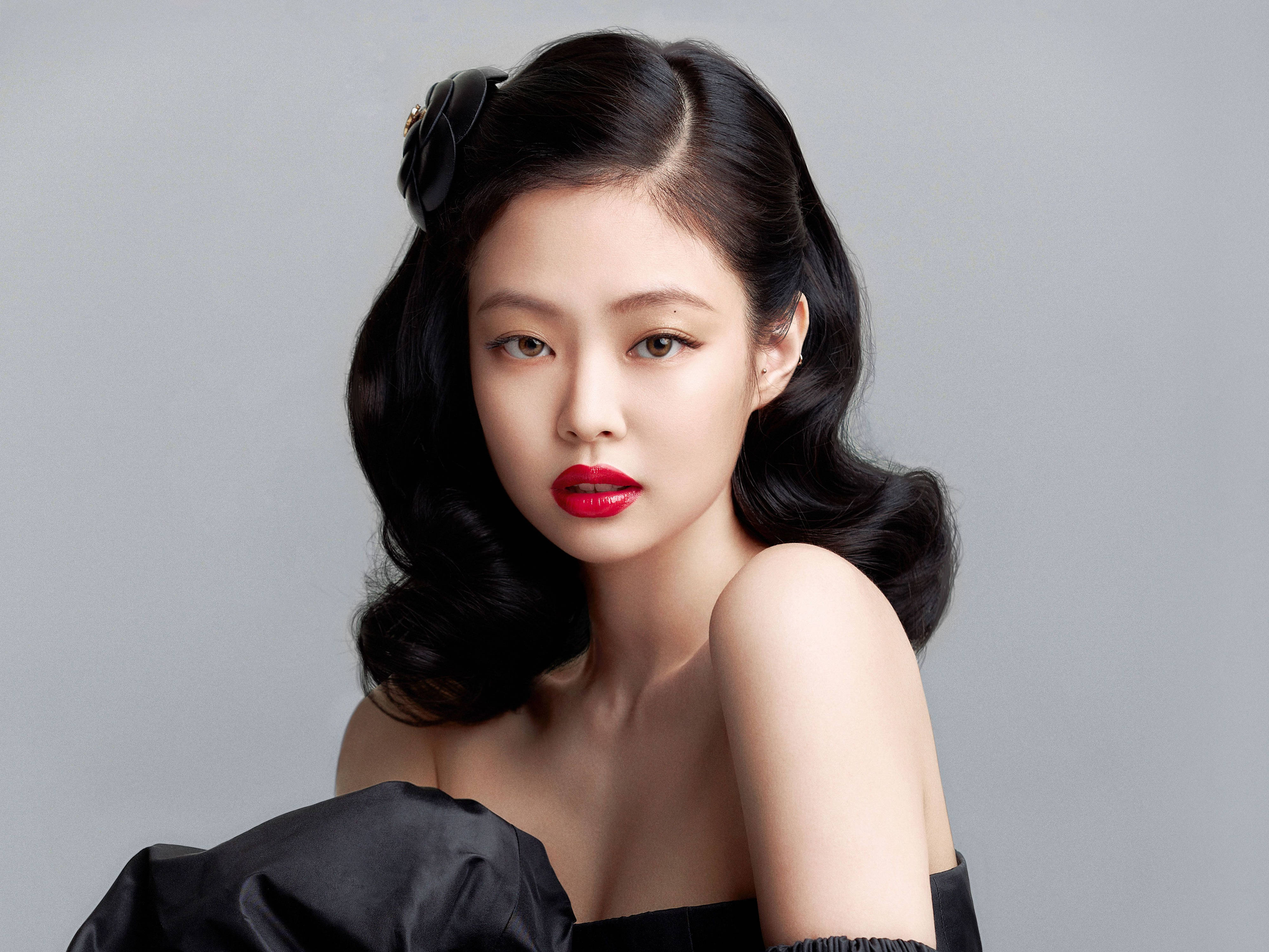 BLACKPINK 桌布 壁紙 — 一位擁有光澤黑色波浪髮型和鮮豔紅唇的女性，直視著柔和的灰色背景。