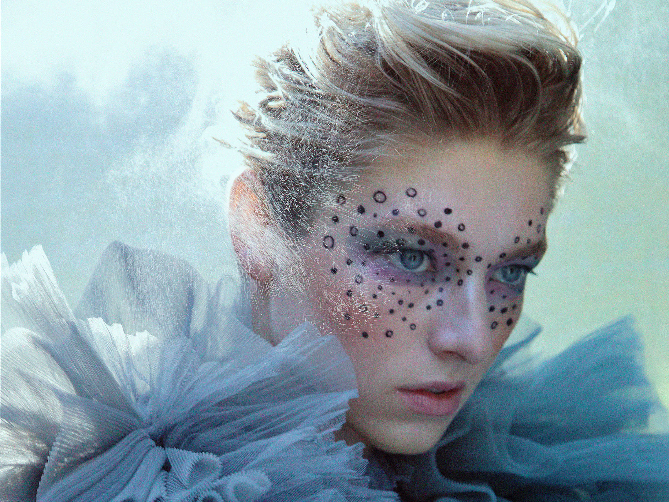 Hunter Schafer 桌布 壁紙 — 一位擁有冰藍色眼睛和黑色圓點妝容的女性，穿著寬大的淡藍色荷葉邊領，透過薄霧凝視。