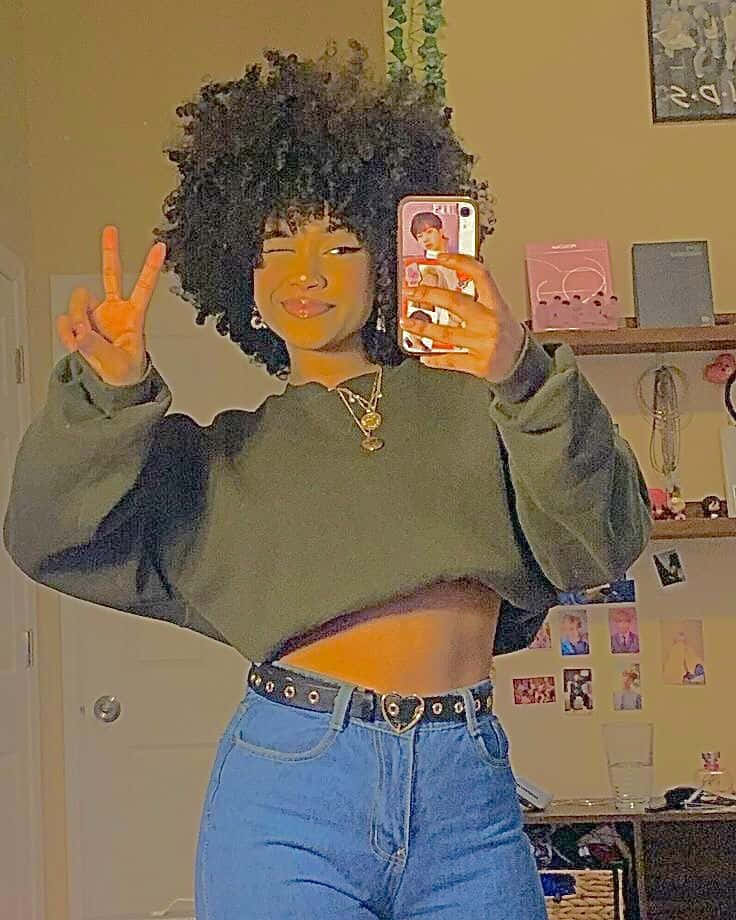 Cute Black Girls 桌布 壁紙 — 一位擁有大型非洲髮型的年輕女性在溫暖照明的房間裡微笑並比出和平手勢，同時對著鏡子自拍。