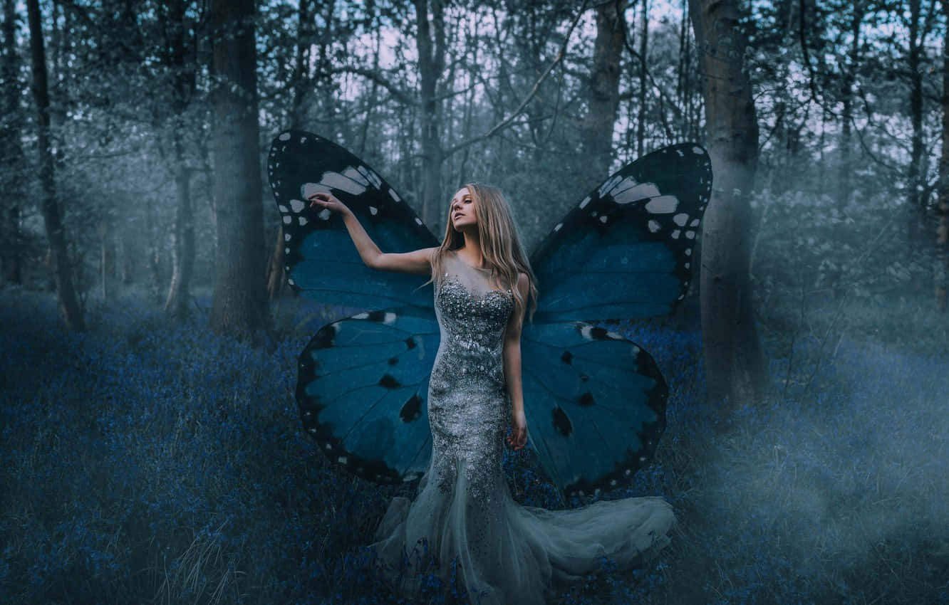 Butterfly Wing Dress 桌布 壁紙 — 一位擁有巨大藍色蝴蝶翅膀的女性優雅地站在充滿藍色花朵的迷霧森林中。
