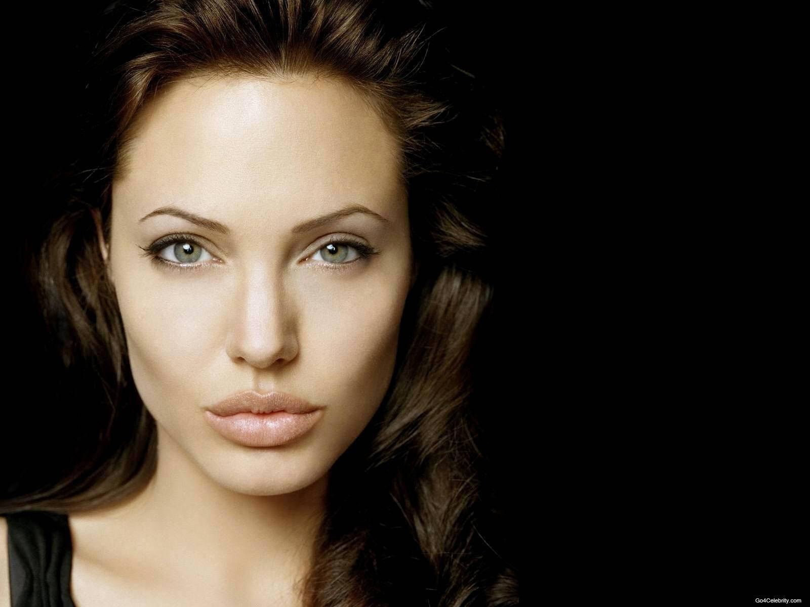 Angelina 桌布 壁紙 — 一位擁有引人注目的綠色眼睛和深色頭髮的女性的特寫肖像，背景為純黑色。
