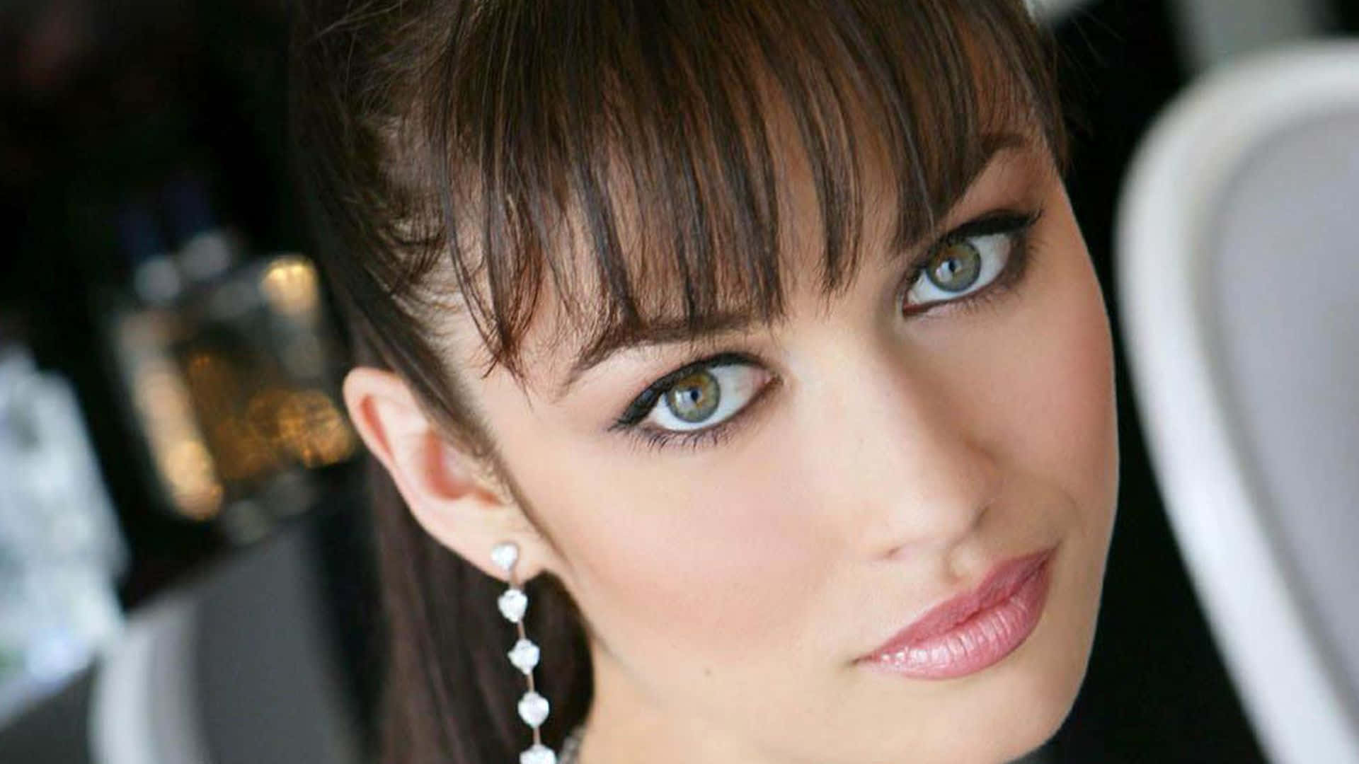 Olga Kurylenko 桌布 壁紙 — 一位擁有引人注目的綠色眼睛和珍珠耳環的女性特寫肖像，直視觀眾。