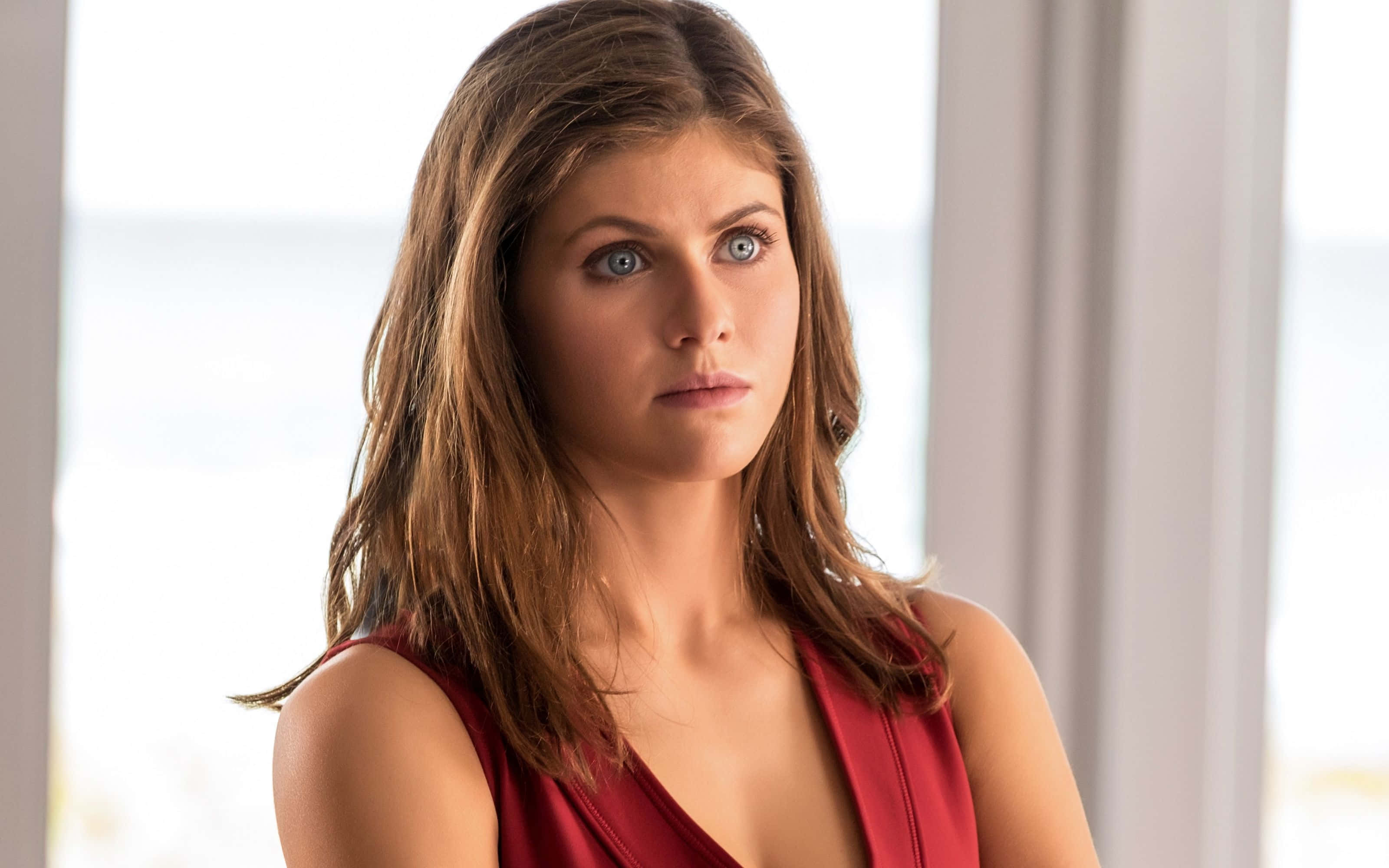 Alexandra Daddario 桌布 壁紙 — 一位擁有引人注目的藍眼睛和棕色頭髮的女性，穿著紅色連衣裙，在明亮的窗邊若有所思地凝視。
