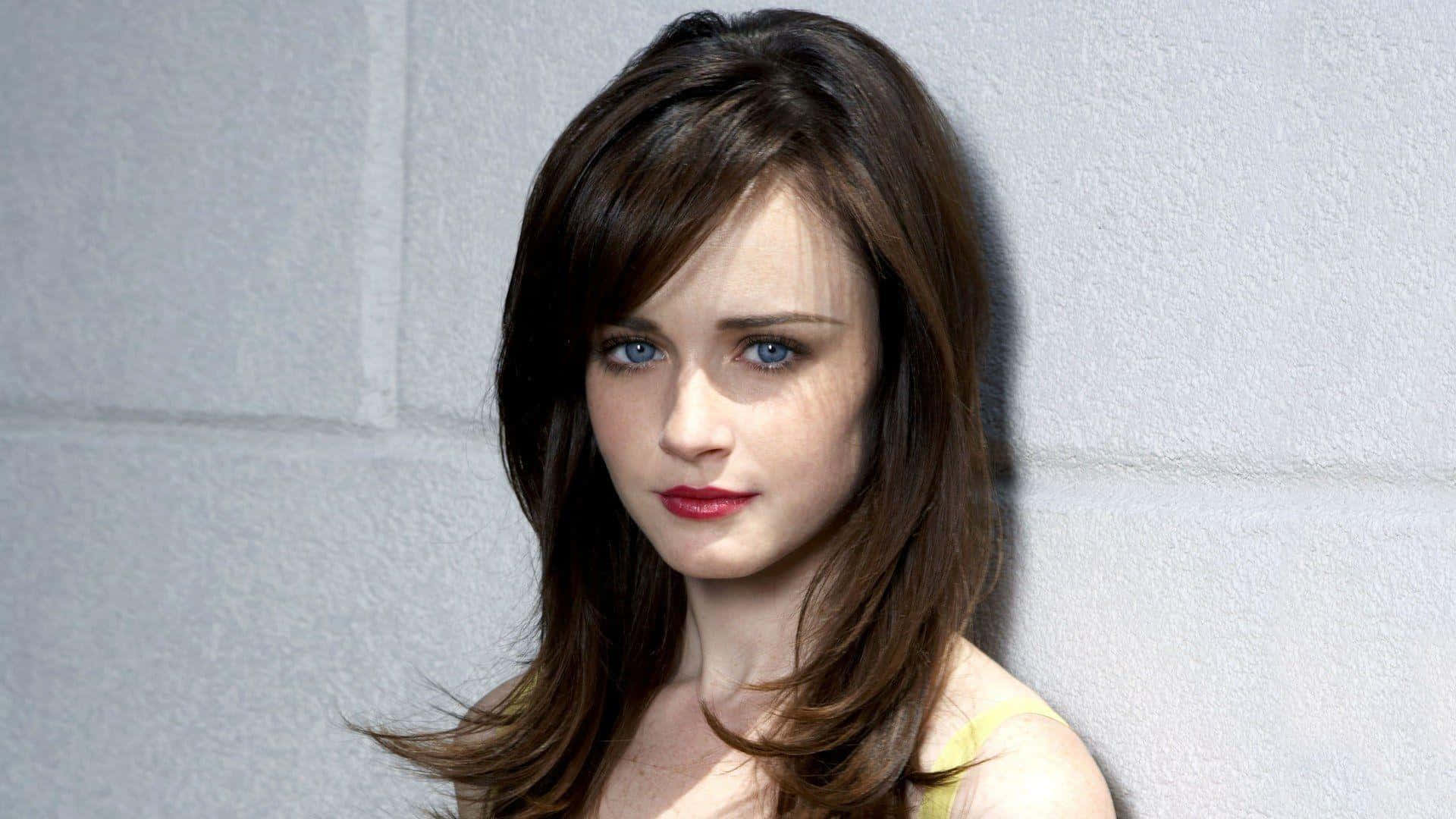 Alexis Bledel 桌布 壁紙 — 一位擁有引人注目的藍色眼睛和棕色頭髮的女性靠著紋理灰色牆壁，穿著黃色上衣和紅色唇膏。