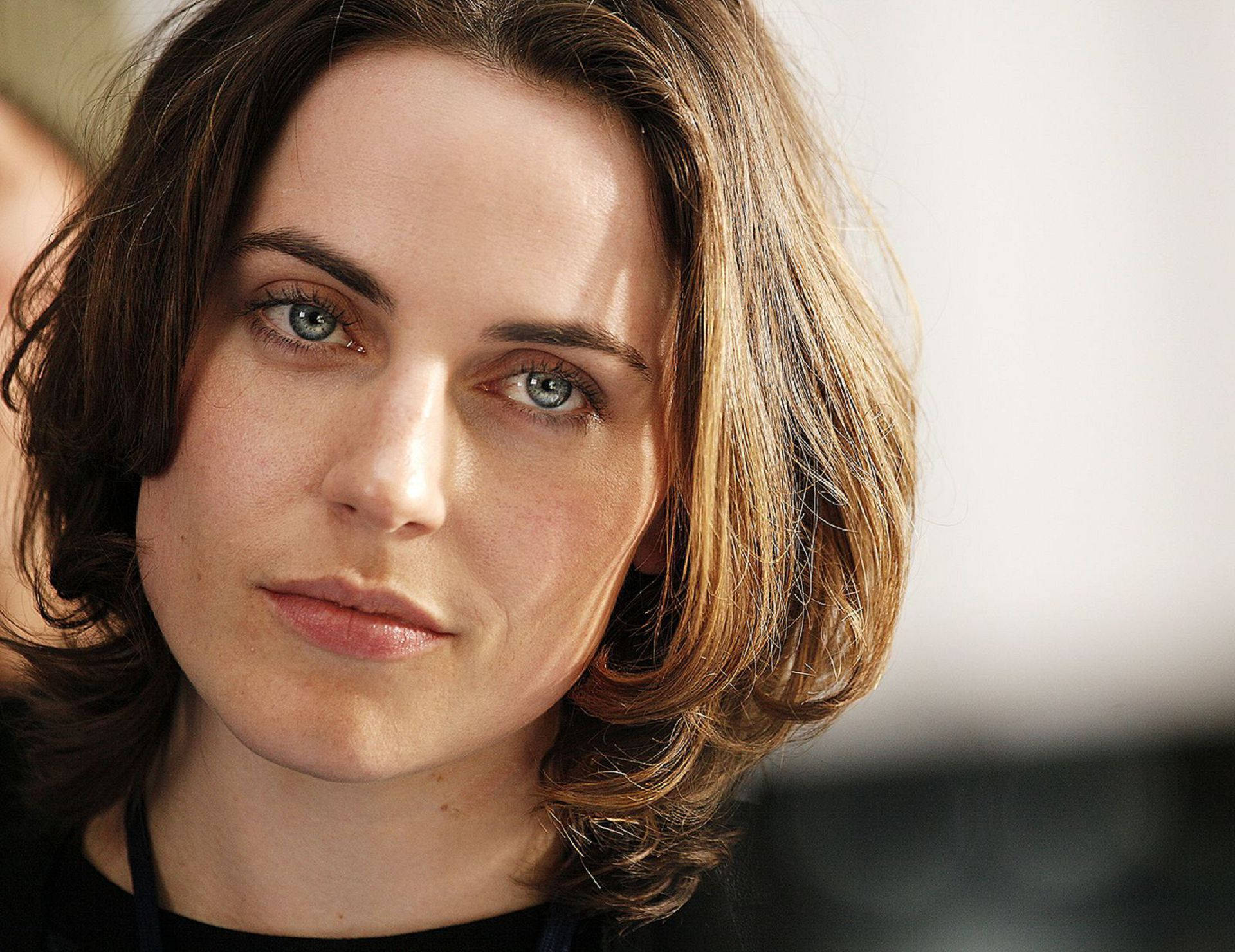 Antje Traue 桌布 壁紙 — 一位擁有引人注目的藍色眼睛和波浪棕色頭髮的女性的特寫肖像，面無表情地直視鏡頭。