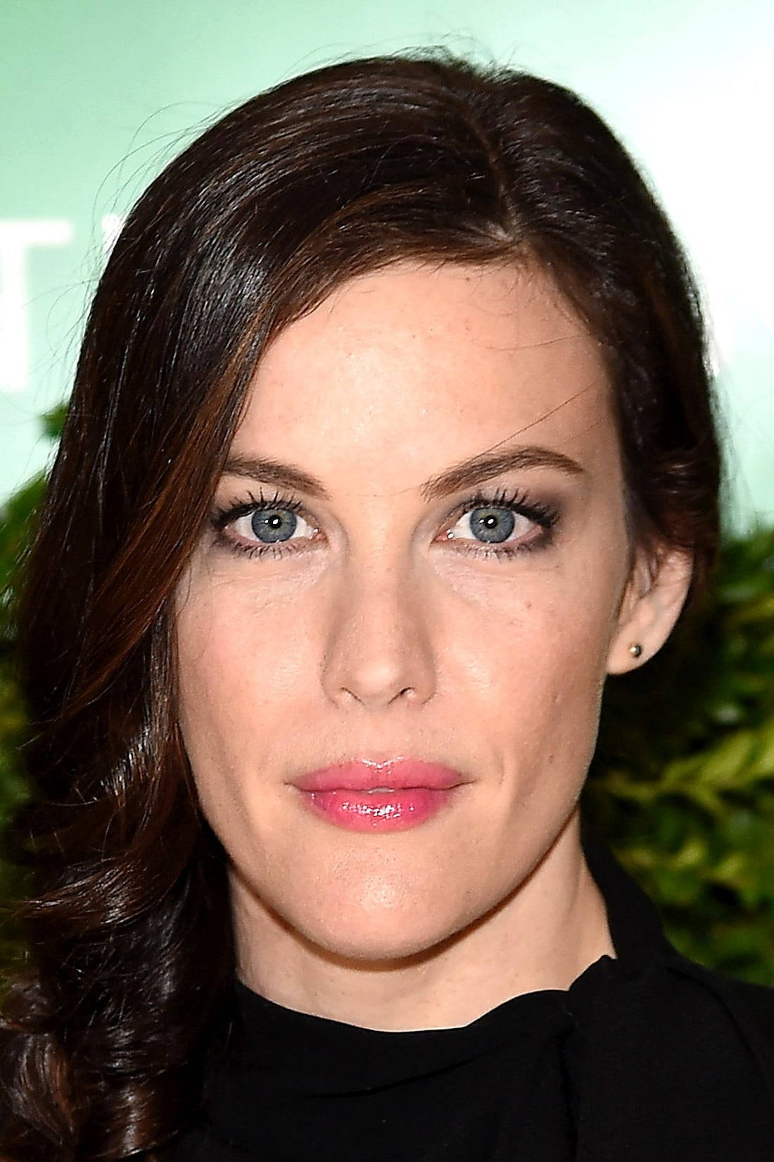 Liv Tyler 桌布 壁紙 — 一位擁有引人注目的藍色眼睛和深色頭髮的女性，在柔和的綠色背景下的特寫肖像。