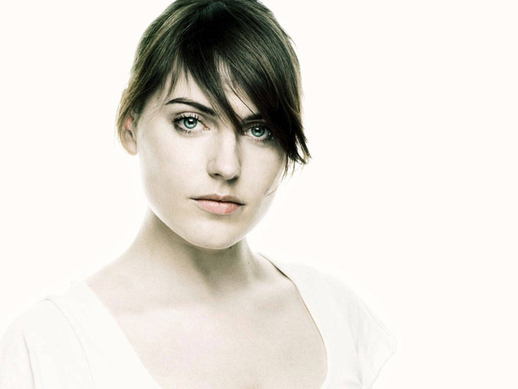 Antje Traue 桌布 壁紙 — 一位擁有引人注目的藍色眼睛和深色頭髮的女性，在純白色背景下直視鏡頭。