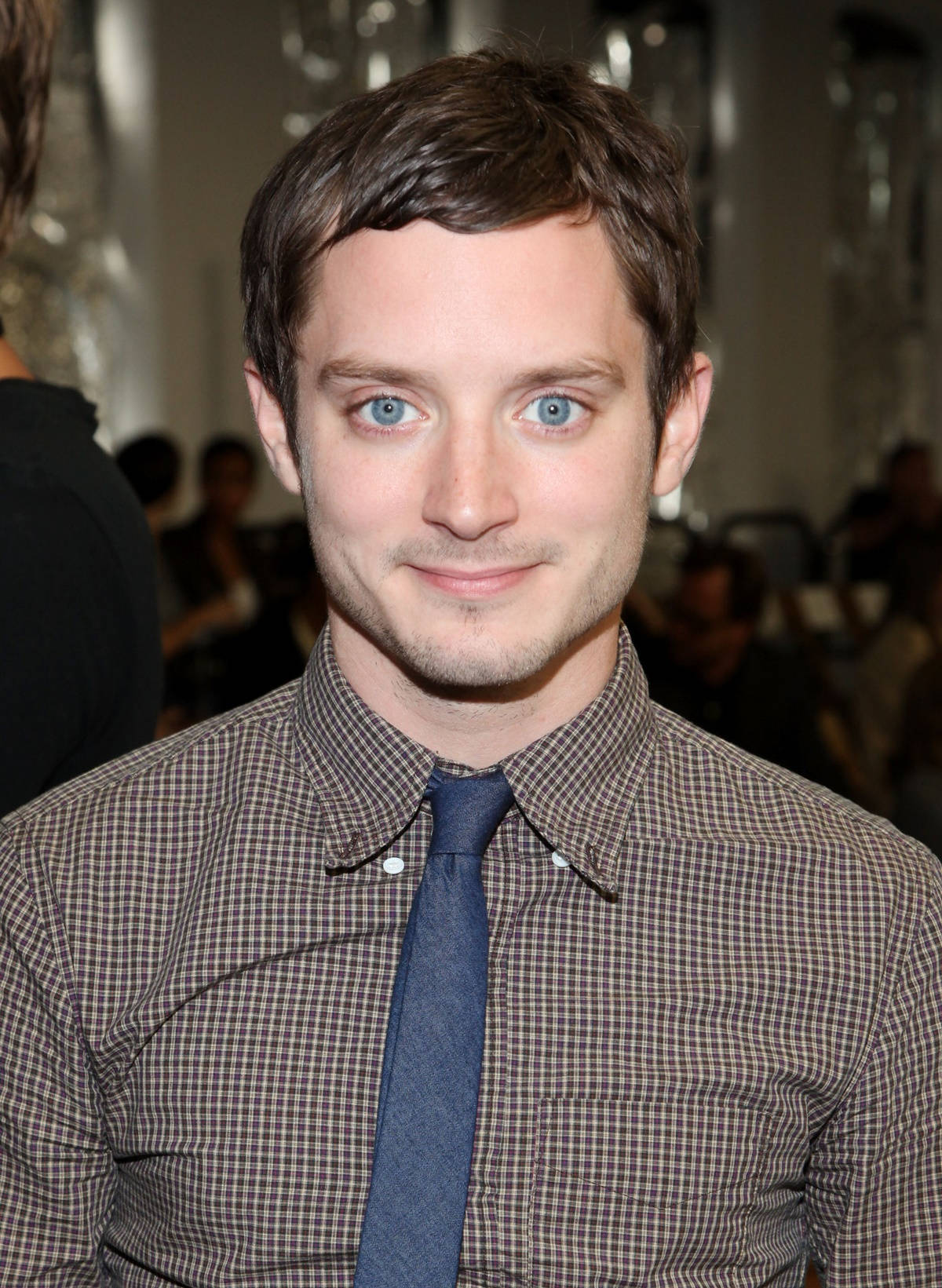 Celebrity 桌布 壁紙 — 一位擁有引人注目的藍色眼睛和短棕髮的男人，穿著格紋襯衫和海軍藍領帶，溫柔地微笑。