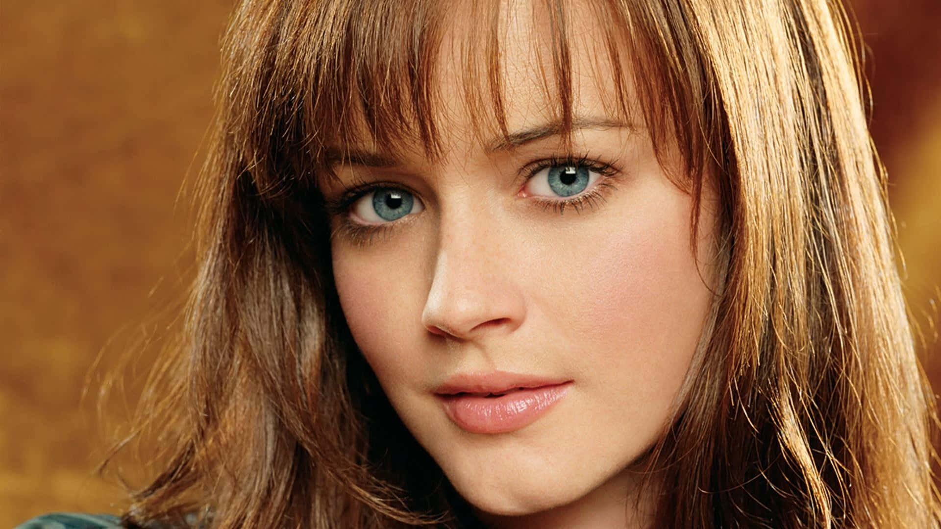 Alexis Bledel 桌布 壁紙 — 一位擁有引人注目的藍色眼睛和赤褐色頭髮的女性，在溫暖的金色背景下的特寫肖像。