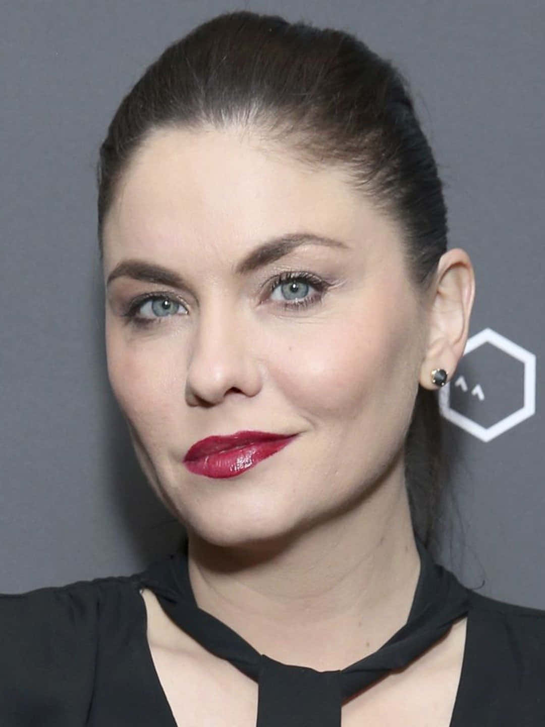 jodi lyn o'keefe 桌布 壁紙 — 一位擁有引人注目的藍色眼睛和鮮豔紅唇的女性，在灰色背景下的特寫肖像。
