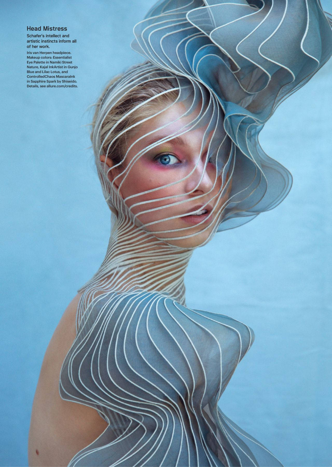 Hunter Schafer 桌布 壁紙 — 一位擁有引人注目的藍色眼睛的女性，部分被流動的半透明藍色布料和纏繞在她頭部和肩膀的白色線條遮擋，背景為純藍色。