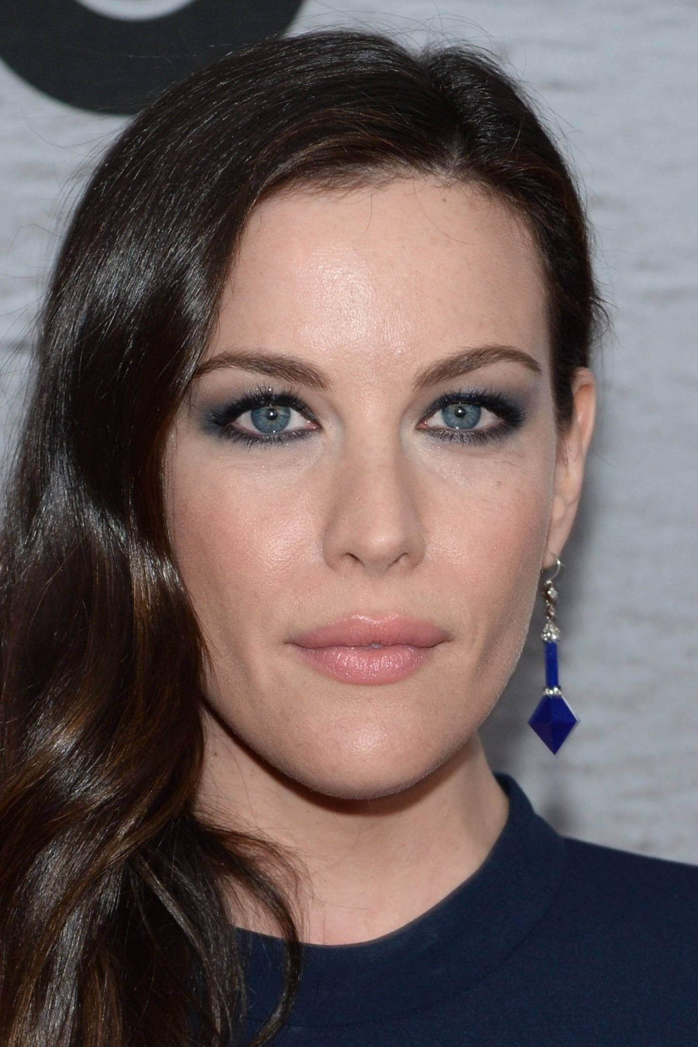 Liv Tyler 桌布 壁紙 — 一位擁有引人注目藍眼睛、深色煙燻妝和醒目藍色吊墜耳環的女子的特寫肖像。
