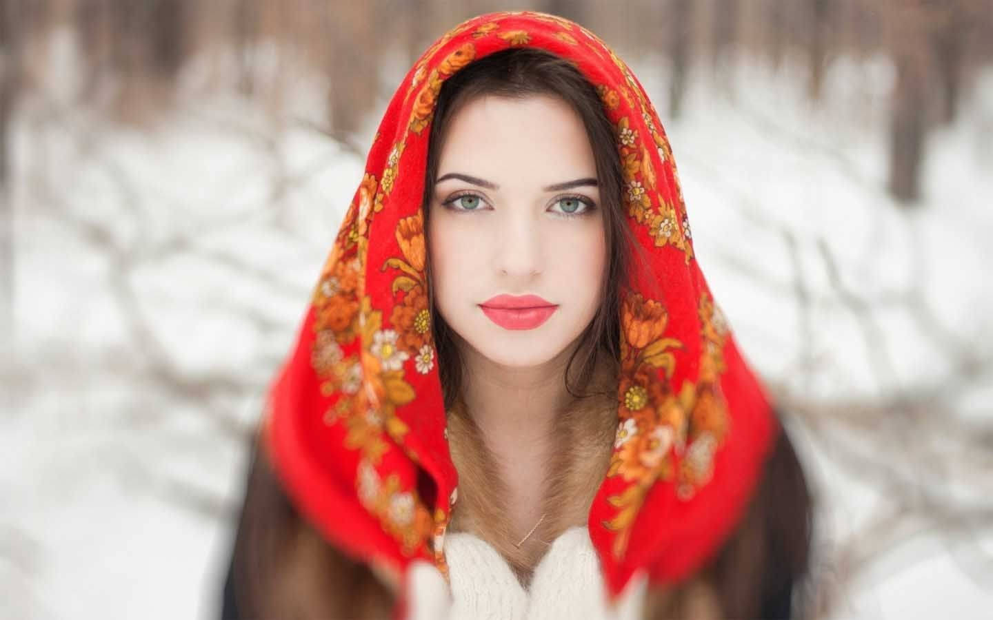 muslim 桌布 壁紙 — 一位擁有引人注目藍眼睛的女性，在白雪皚皚的冬季森林背景下，戴著鮮豔的紅色花卉頭巾。
