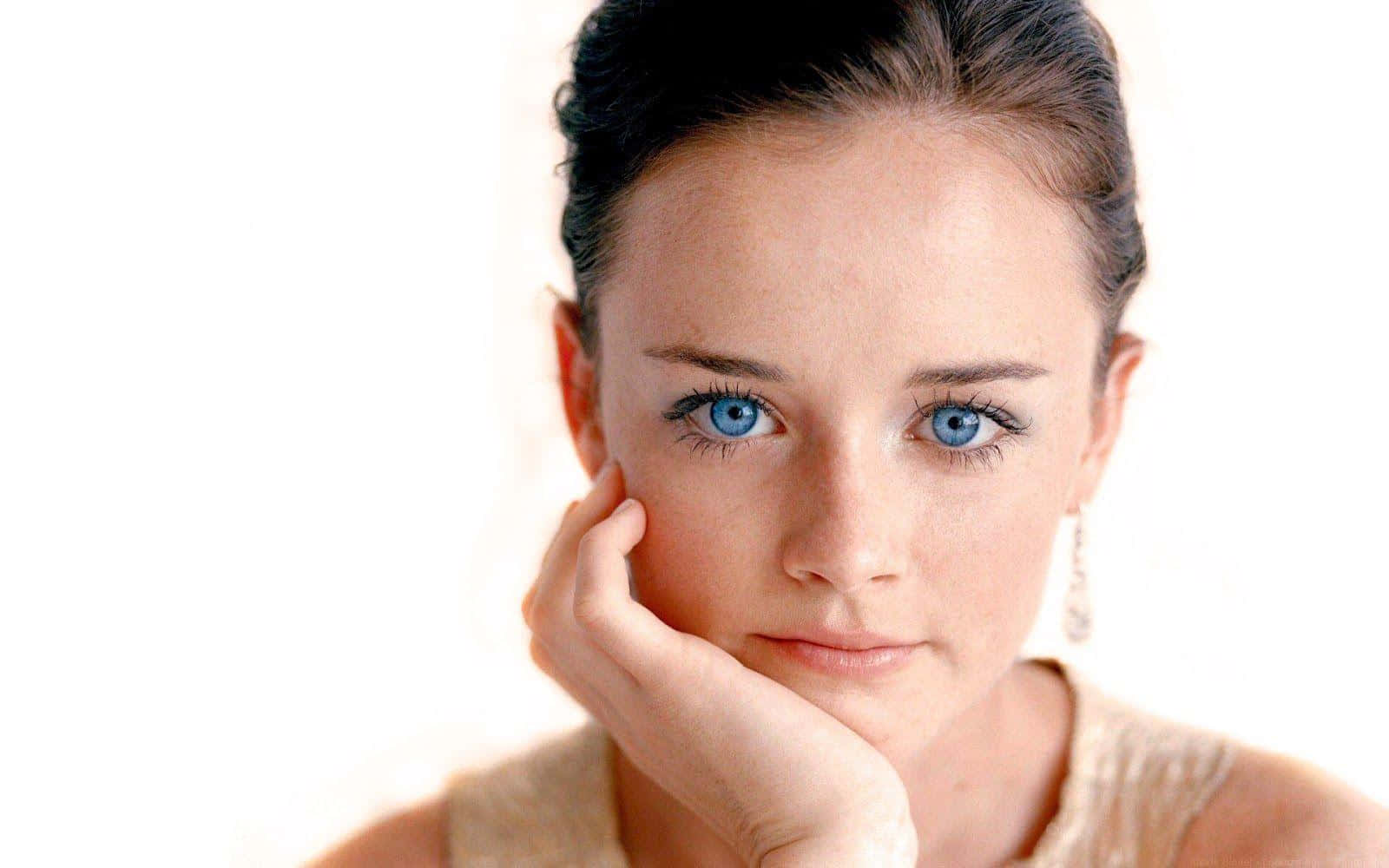 Alexis Bledel 桌布 壁紙 — 一位擁有引人注目藍眼睛的女性，在明亮的白色背景前將下巴擱在手上的特寫肖像。