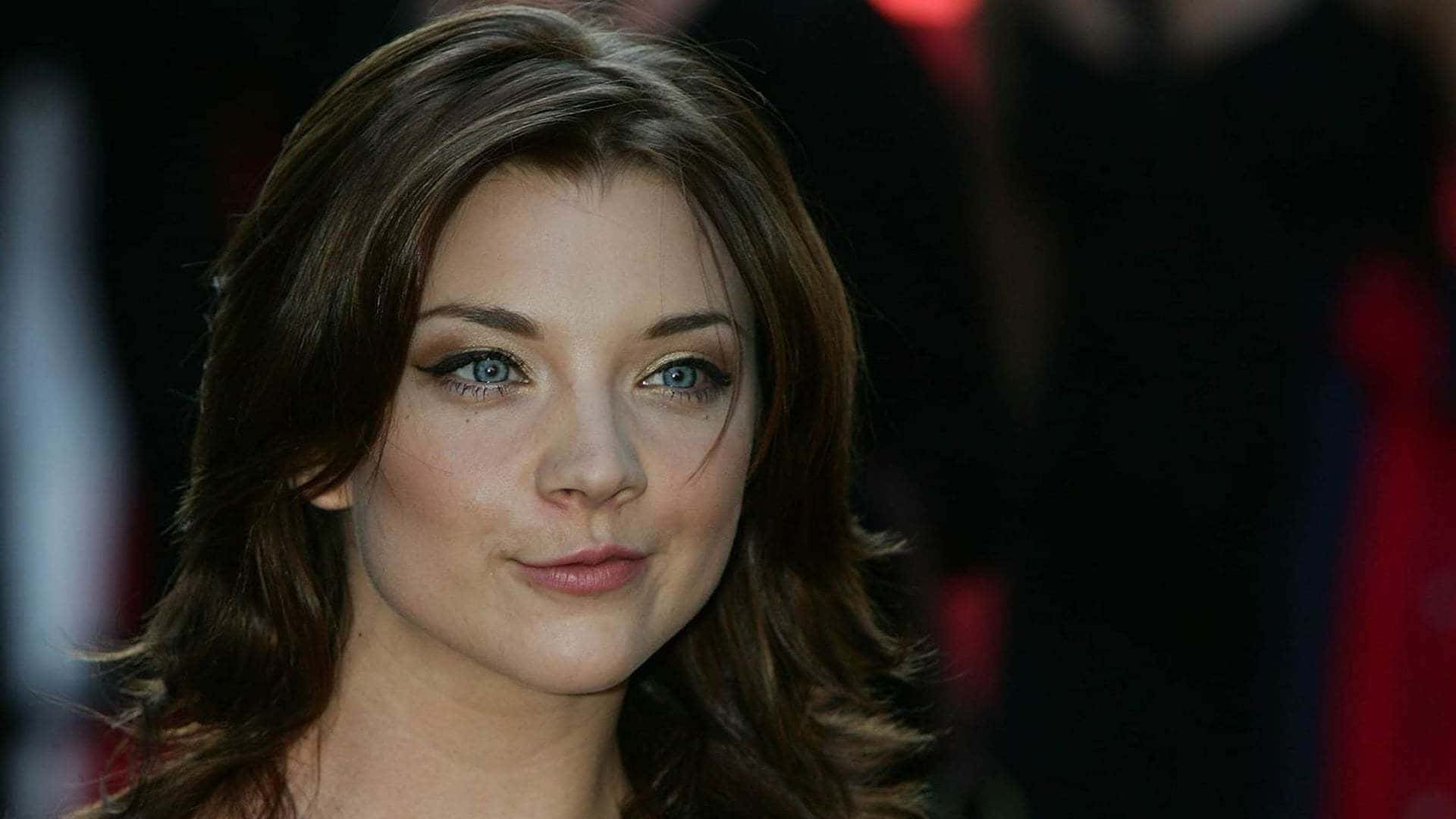 natalie dormer 桌布 壁紙 — 一位擁有引人注目藍色眼睛和波浪棕色頭髮的女性特寫肖像，她帶著溫柔的微笑直視鏡頭。