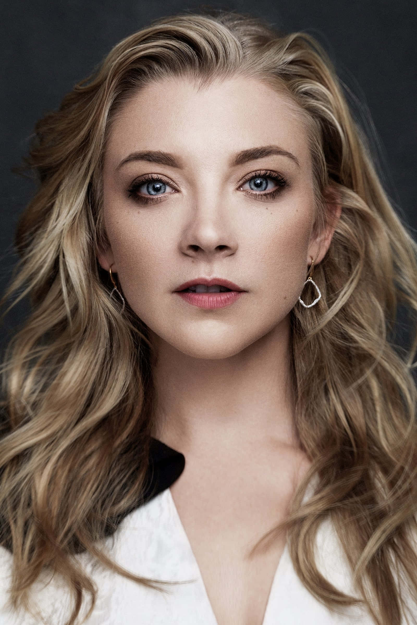 natalie dormer 桌布 壁紙 — 一位擁有引人注目藍色眼睛和波浪金髮的女性，戴著精緻的圈形耳環的特寫肖像。