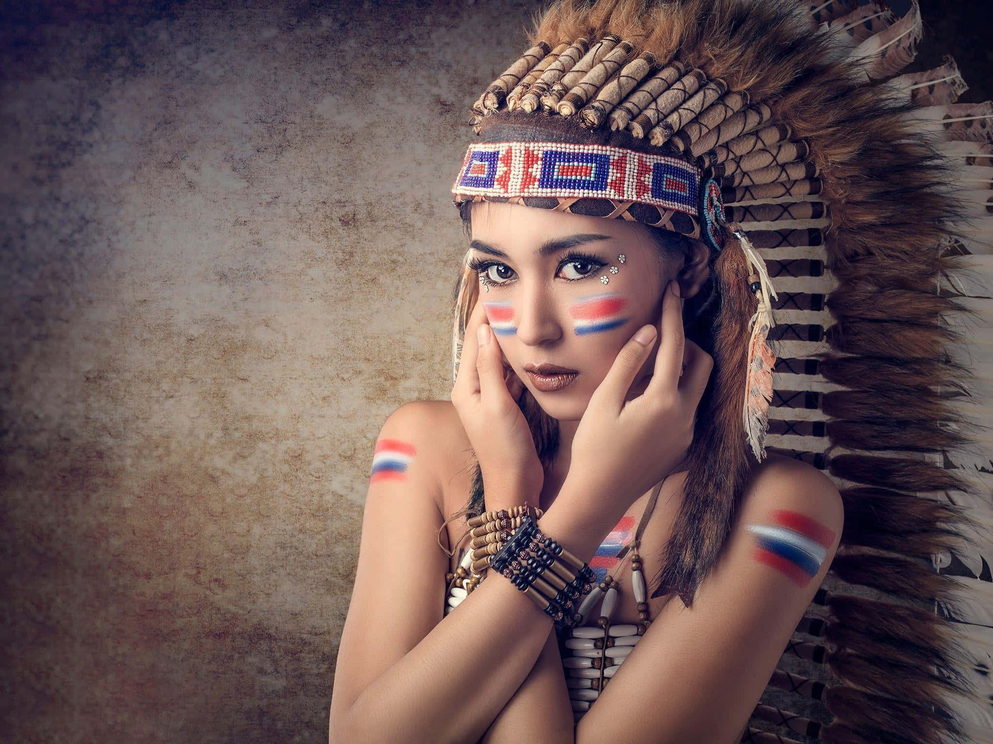 Tribal 桌布 壁紙 — 一位擁有引人注目藍色眼睛的女性，戴著羽毛頭飾，臉上塗有紅、白、藍三色顏料，背景為質感棕色。