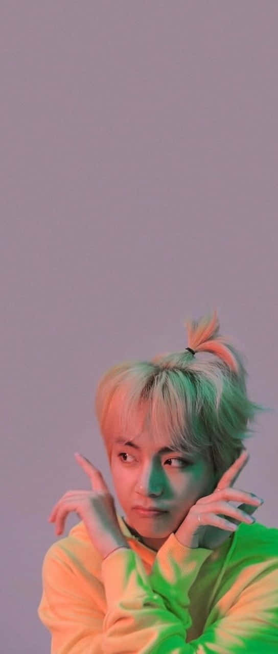 BTS V 動圖 桌布 壁紙 — 一位擁有彩色頭髮和鮮豔連帽衫的年輕男子，在柔和的紫色背景和霓虹燈光下擺姿勢。