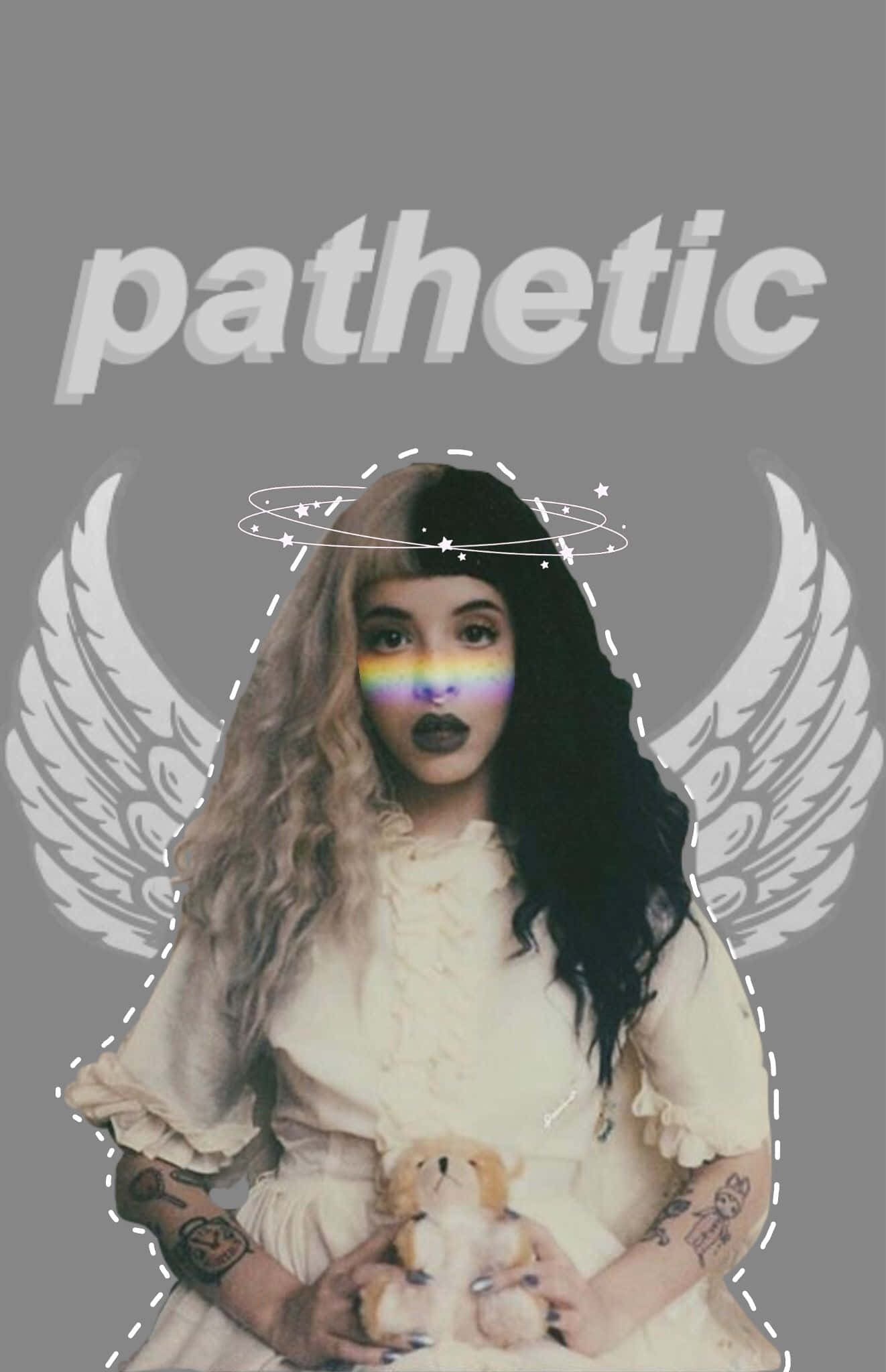 Melanie Martinez Aesthetic 桌布 壁紙 — 一位擁有彩虹眼睛和天使翅膀的年輕女子，在灰色背景前抱著一隻泰迪熊，上面寫著 pathetic。