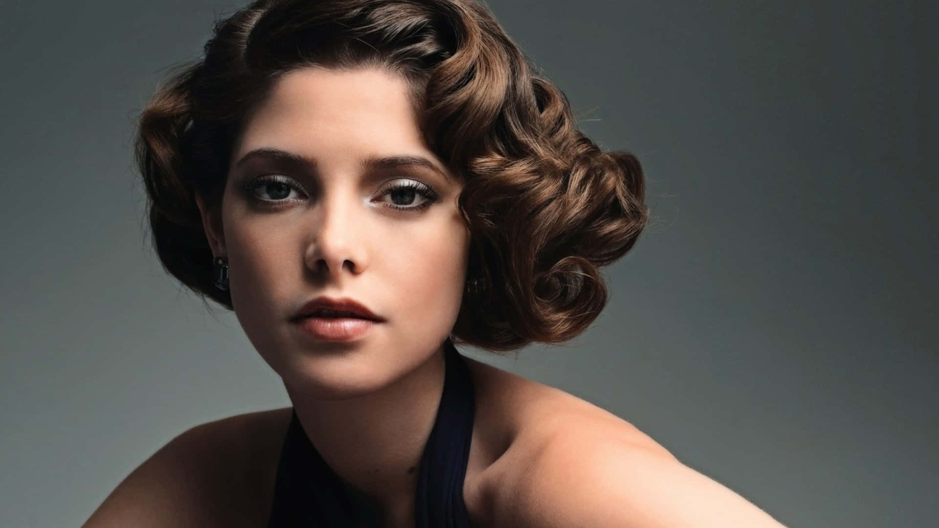 ashley greene 桌布 壁紙 — 一位擁有復古棕色捲髮和煙燻妝眼睛的女性，直視著柔和的灰色背景。