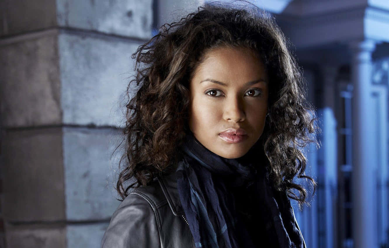 Gugu Mbatha-raw 桌布 壁紙 — 一位擁有捲曲深色頭髮、身穿皮夾克的女性，在冷藍色燈光下對著石建築物凝視。