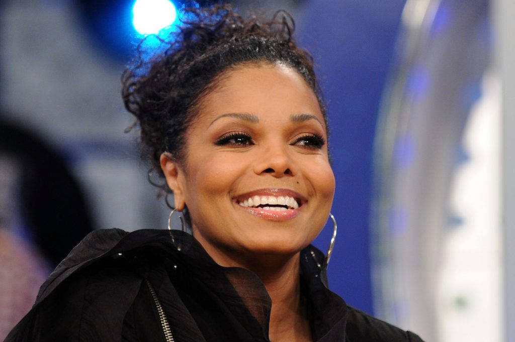 janet jackson 桌布 壁紙 — 一位擁有捲髮和圓環耳環的耀眼女性，身穿黑色外套，在舞台燈光下閃閃發光。